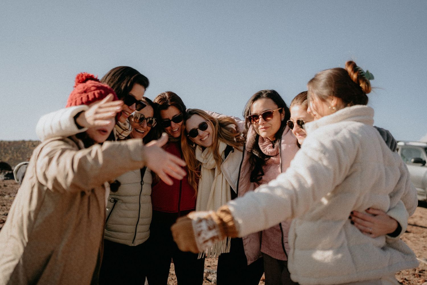 A group huddle of friends sharing a joyful moment in winter coats against mountain backdrop.