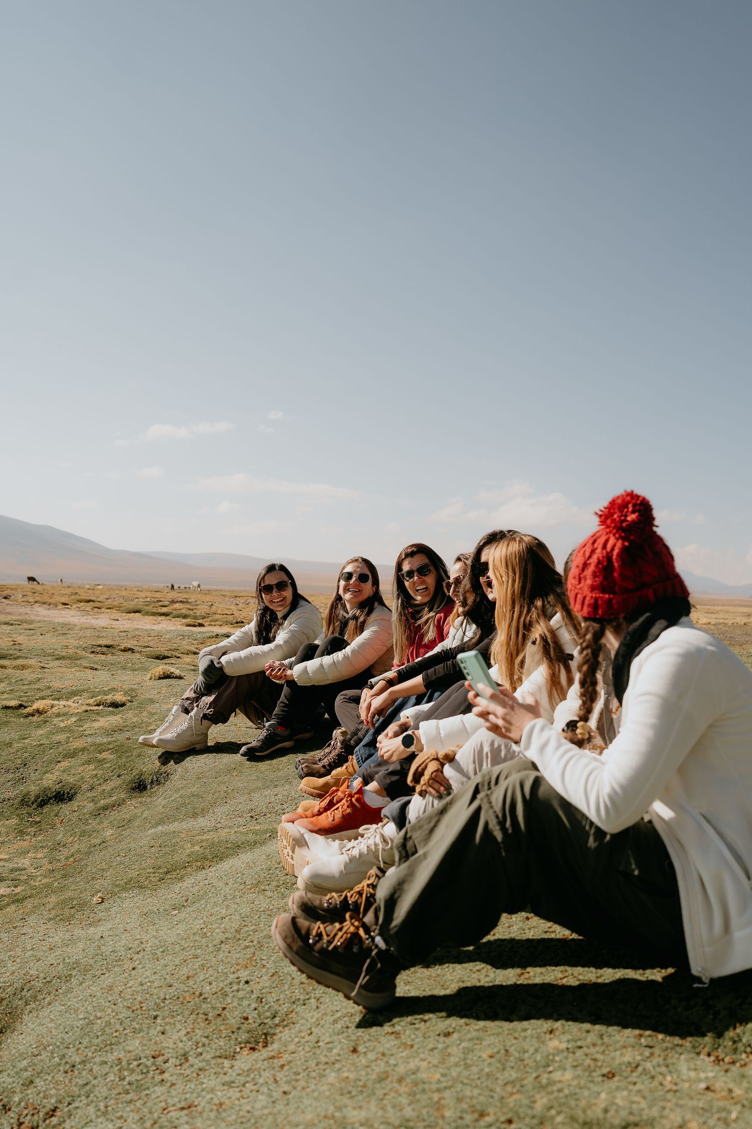 Group of friends in winter wear sitting together on a hillside in an arid landscape.