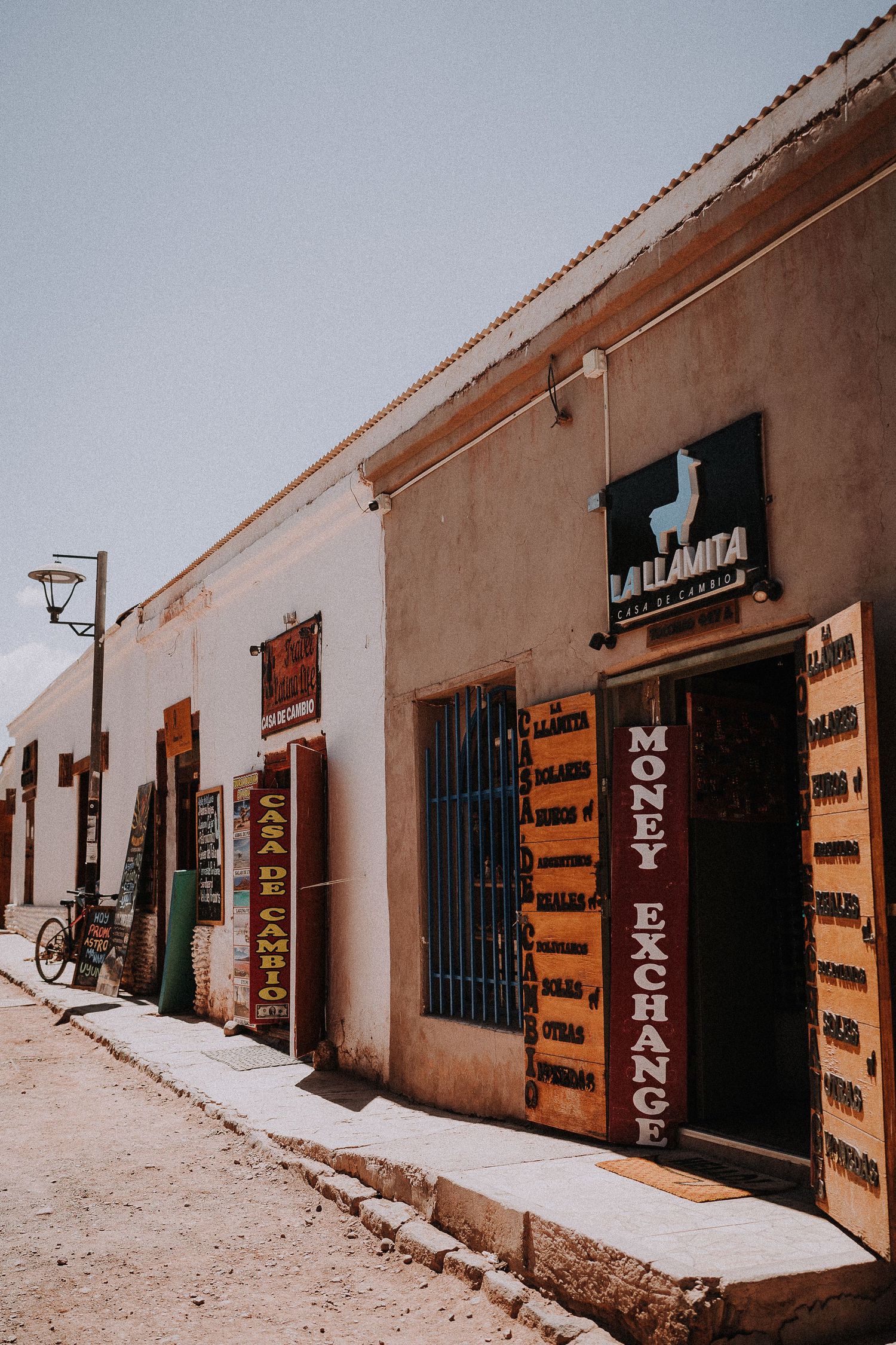 Row of rustic storefronts with wooden doors and adobe walls in a desert town.