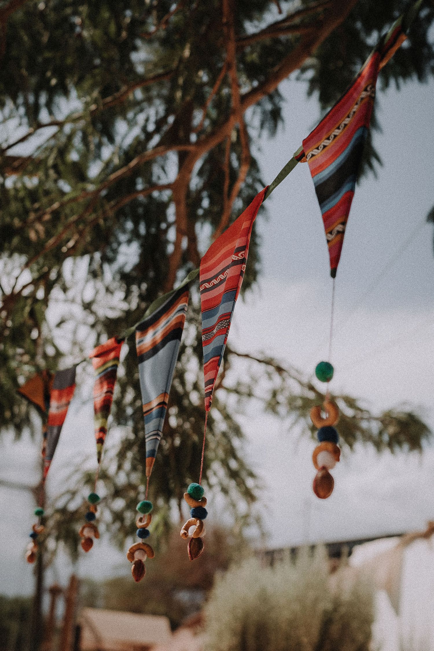 Colorful traditional woven banners with decorative ornaments hanging against pine trees.