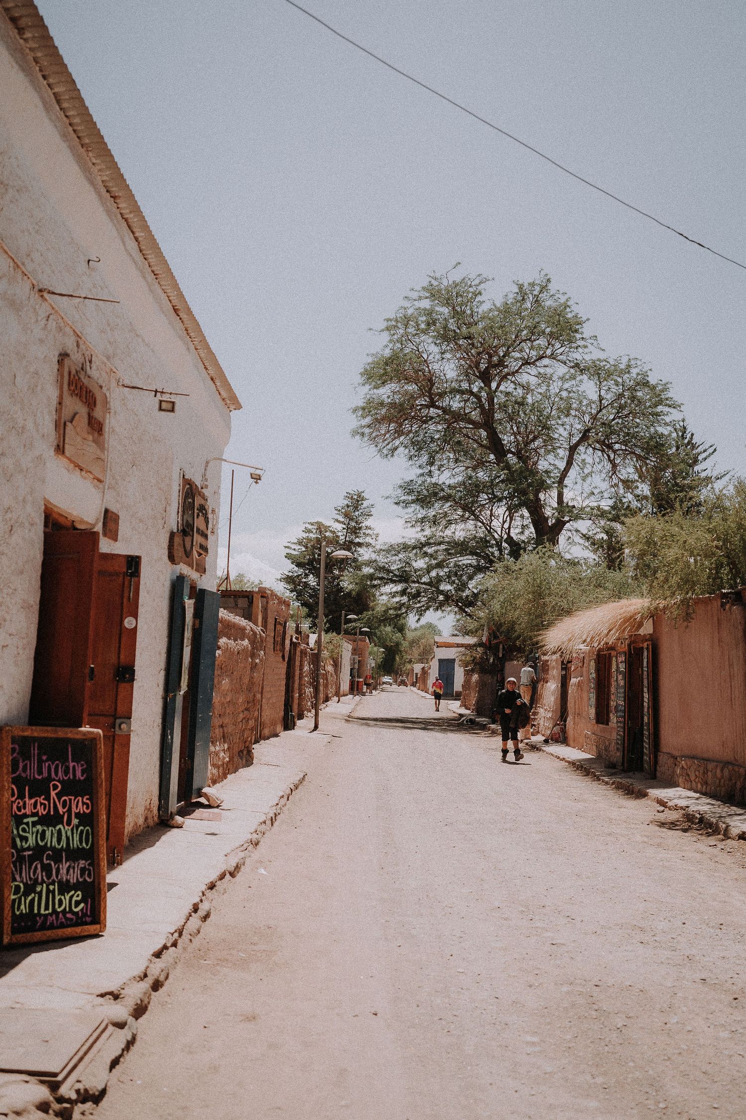 Narrow dirt street lined with adobe buildings and trees in a quaint village.