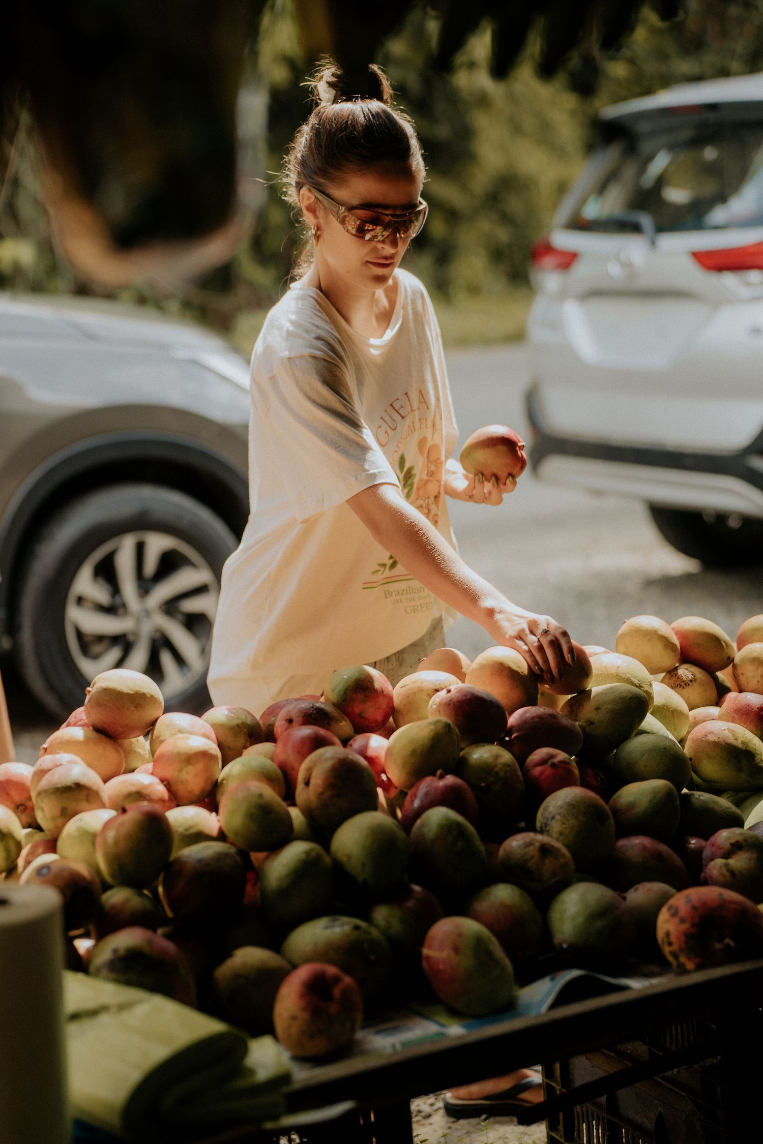 Person sorting through fresh mangoes on outdoor display table.