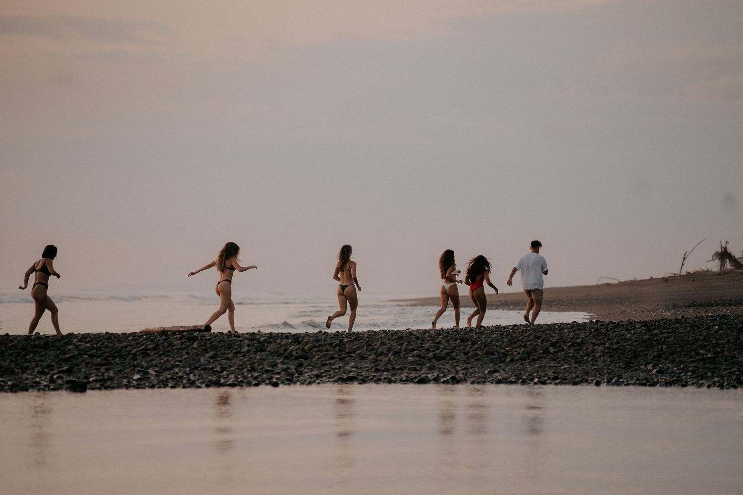 Silhouettes of people walking along a rocky beach during golden hour.