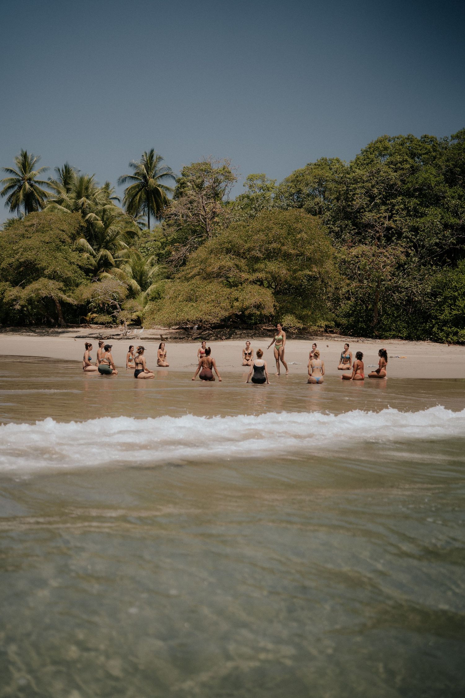 A group enjoys the waves on a tropical beach lined with palm trees and lush vegetation.