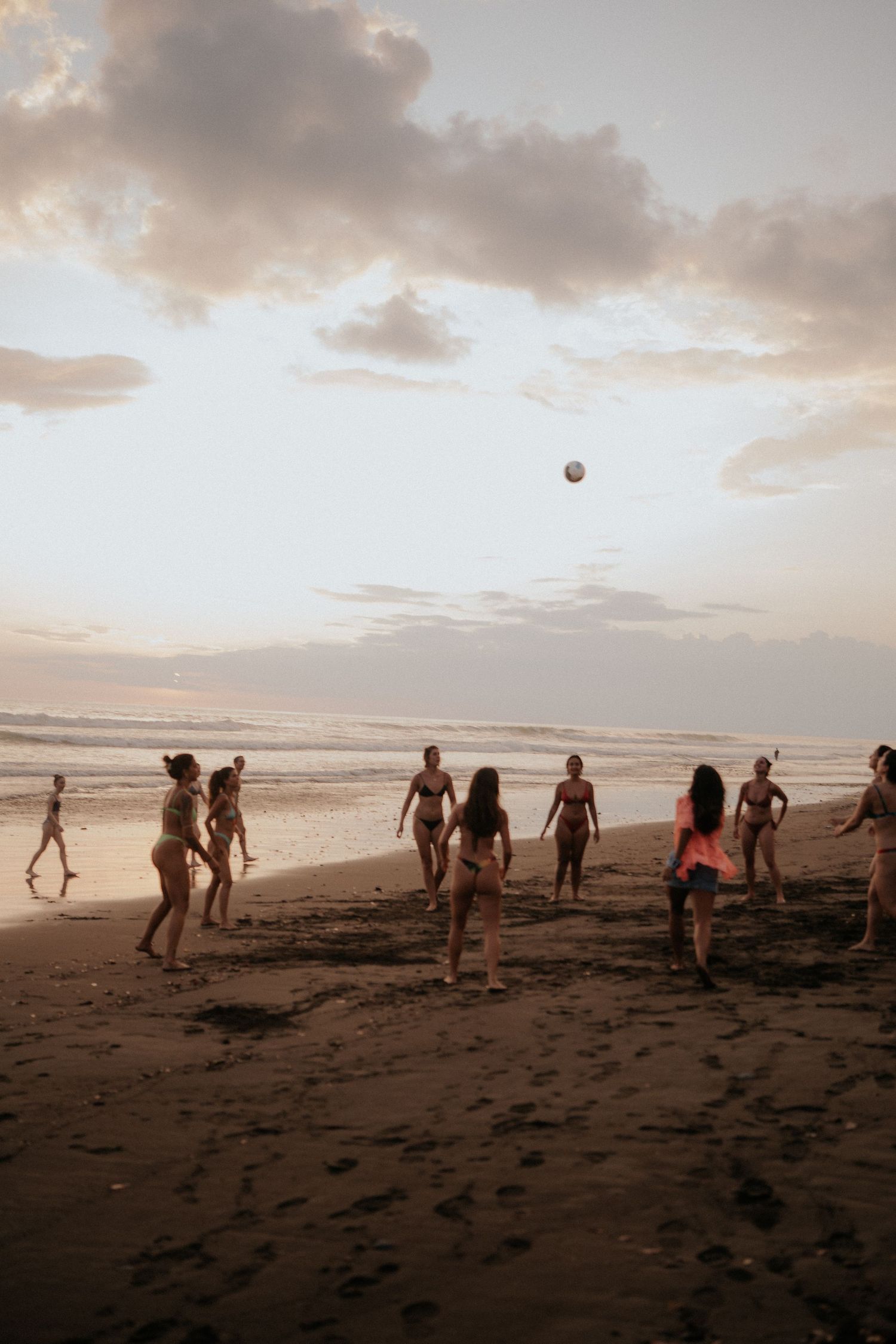 A group plays beach volleyball during sunset on a sandy shore.