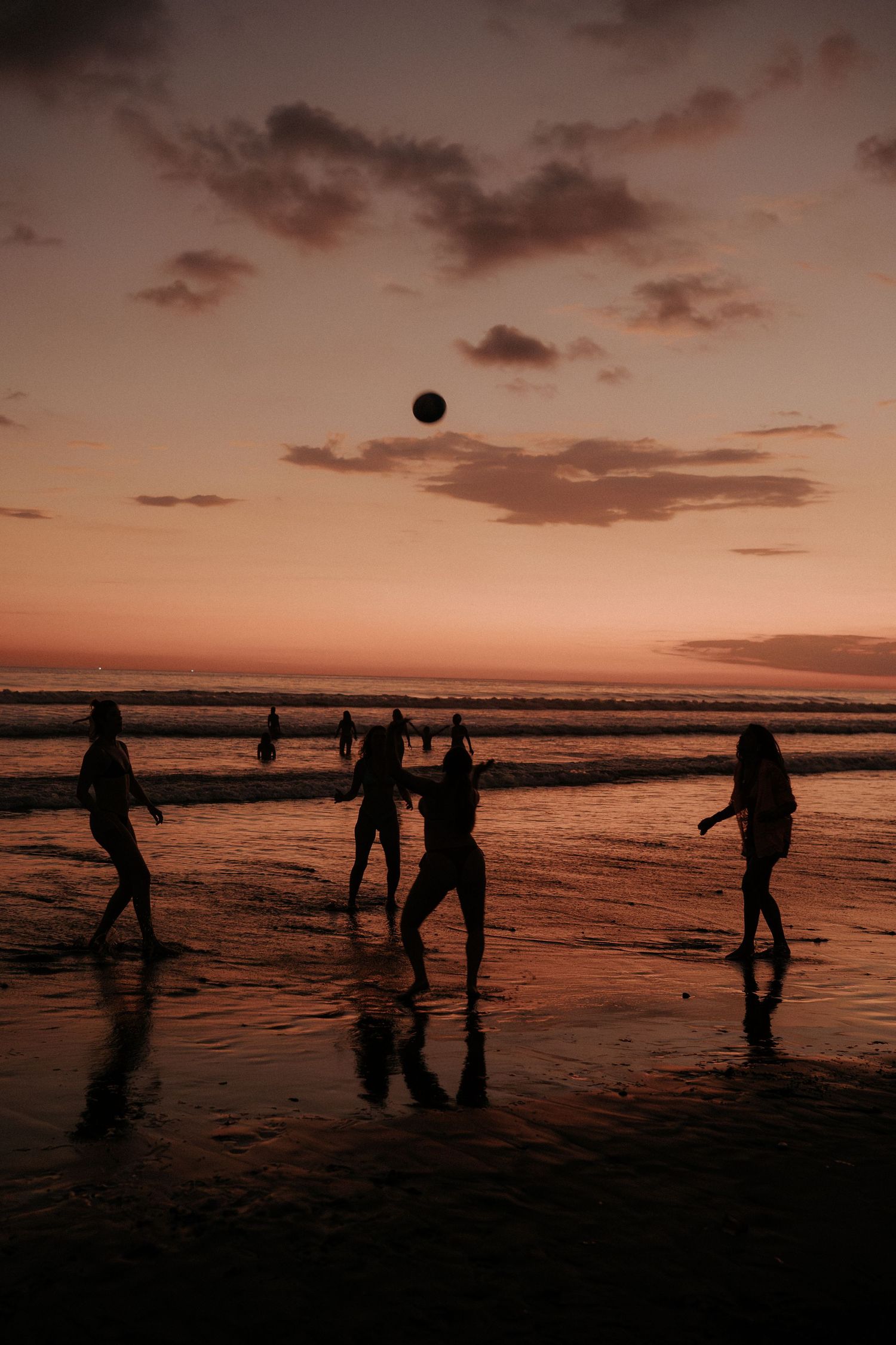 Silhouettes of people playing with a ball on the beach at twilight.