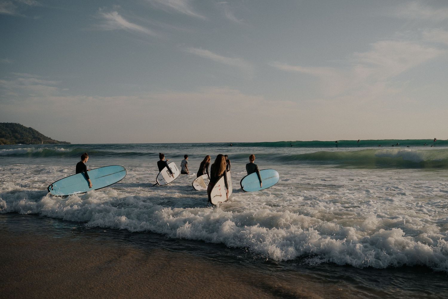 Silhouettes of surfers running through ocean waves during sunset.