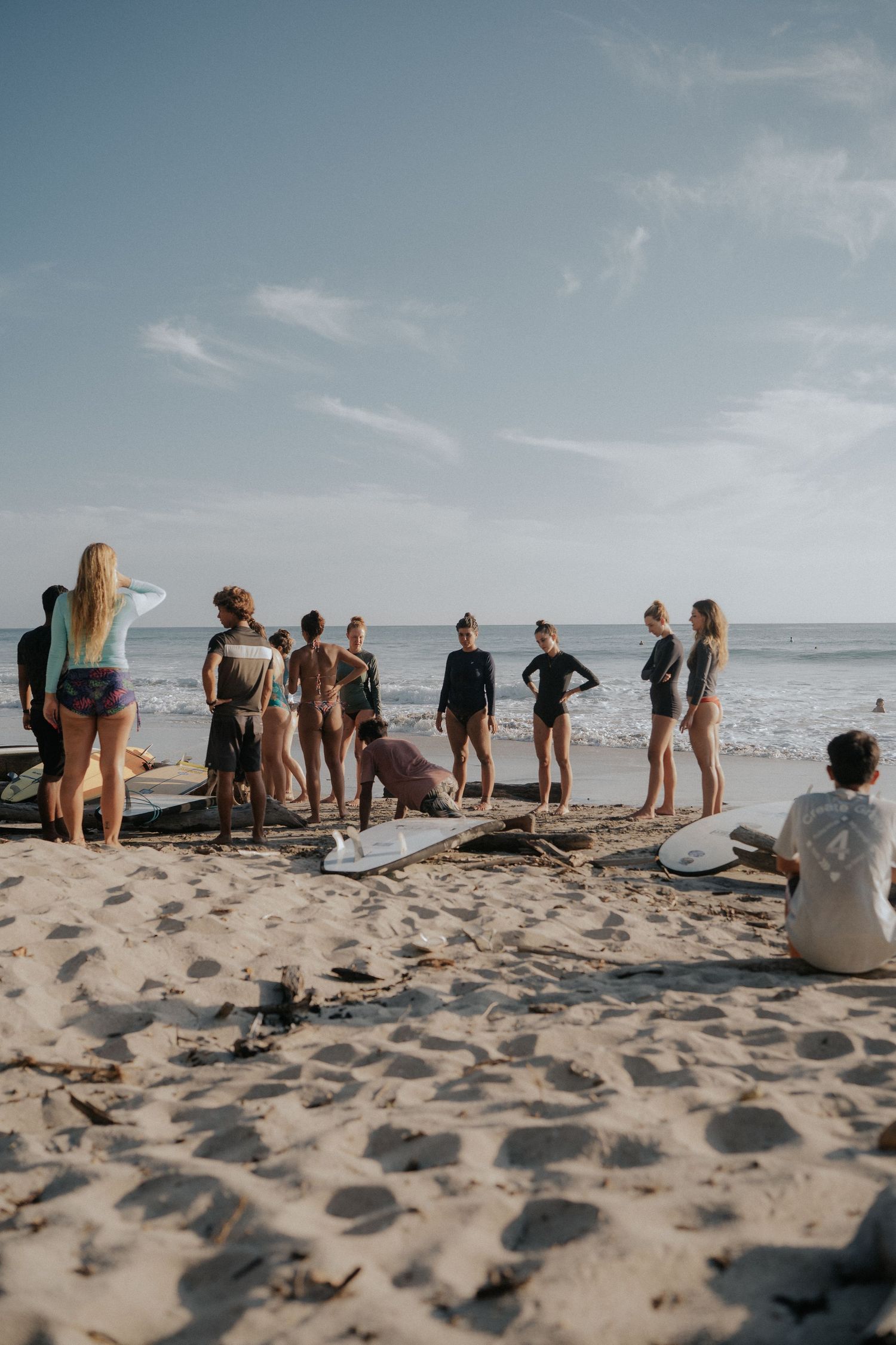 Group of surfers gathered on sandy beach with surfboards during golden hour.