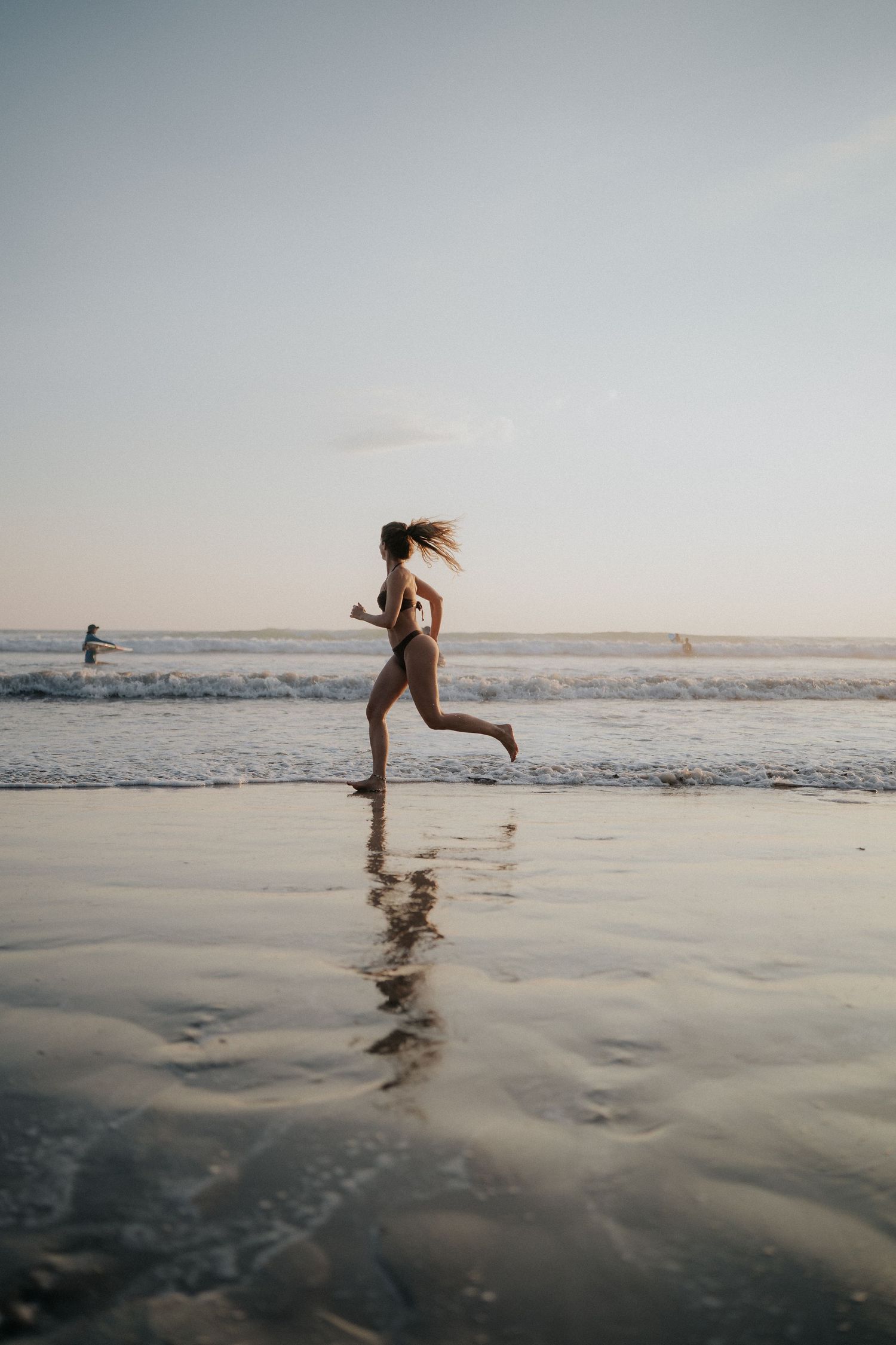 Silhouette of person running and jumping on reflective wet beach at sunset.