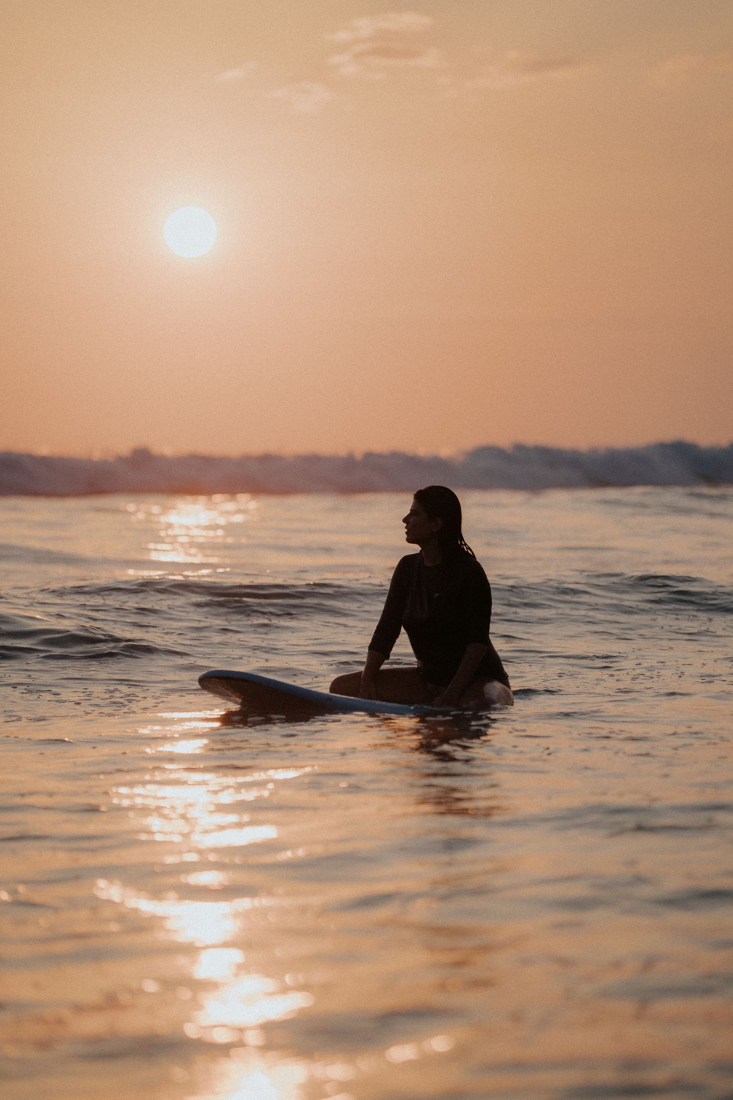 Silhouette of surfer floating in ocean water during golden sunset.