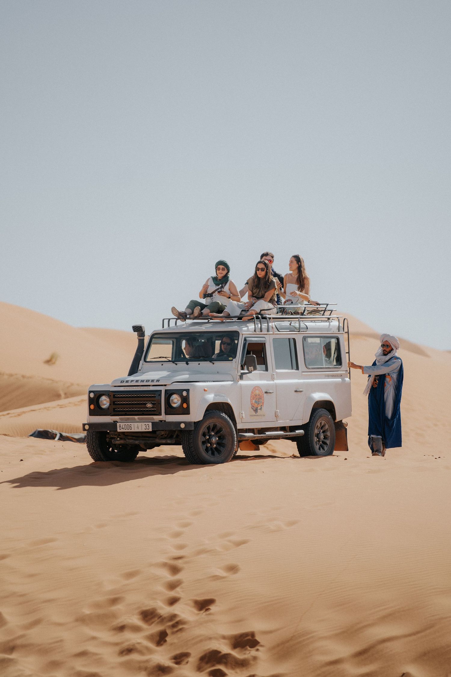 White Land Rover vehicle parked on desert sand dune during safari adventure.