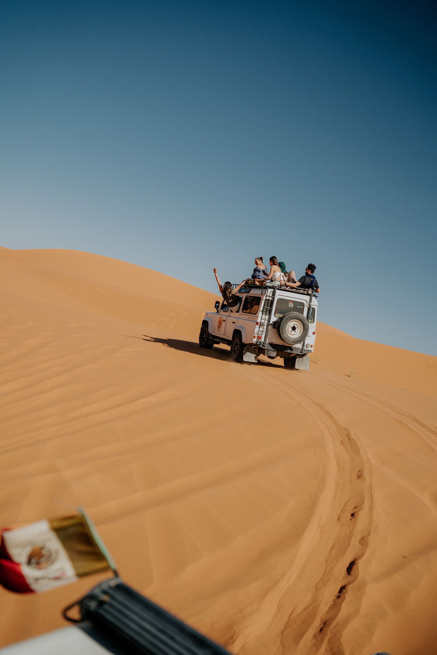 Land Rover vehicle climbing sand dunes in a desert against blue sky.