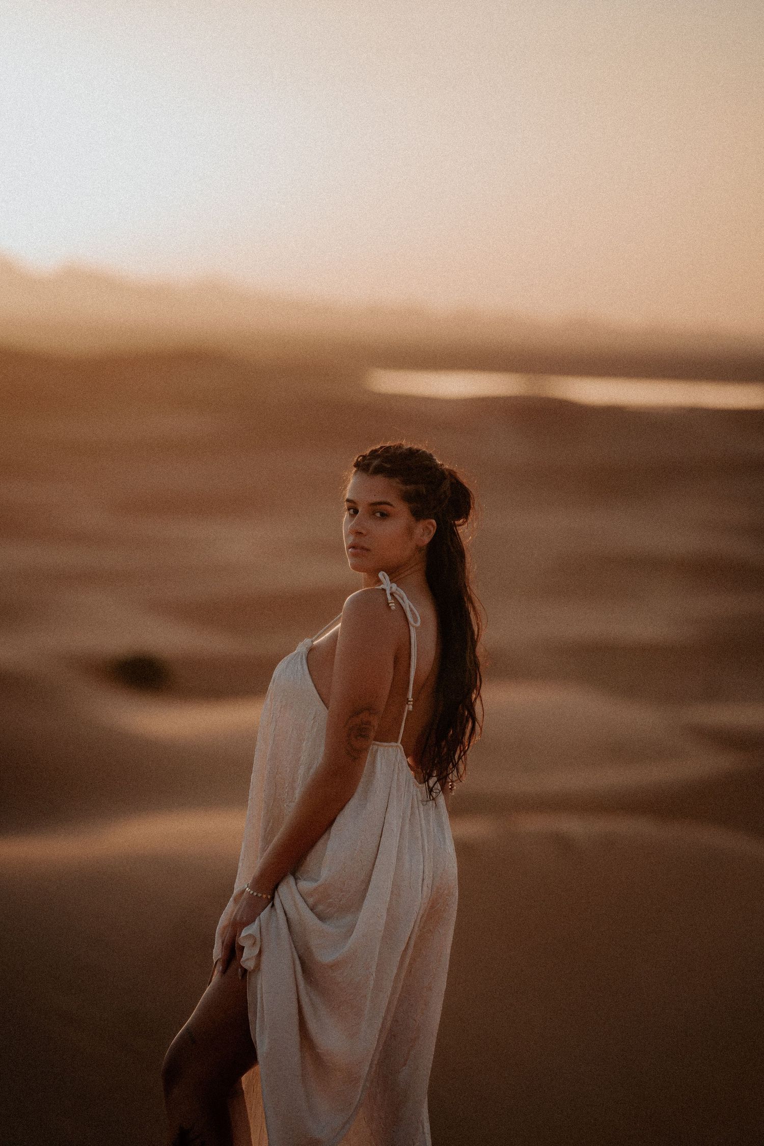 Person in flowing white dress poses against desert sunset landscape.