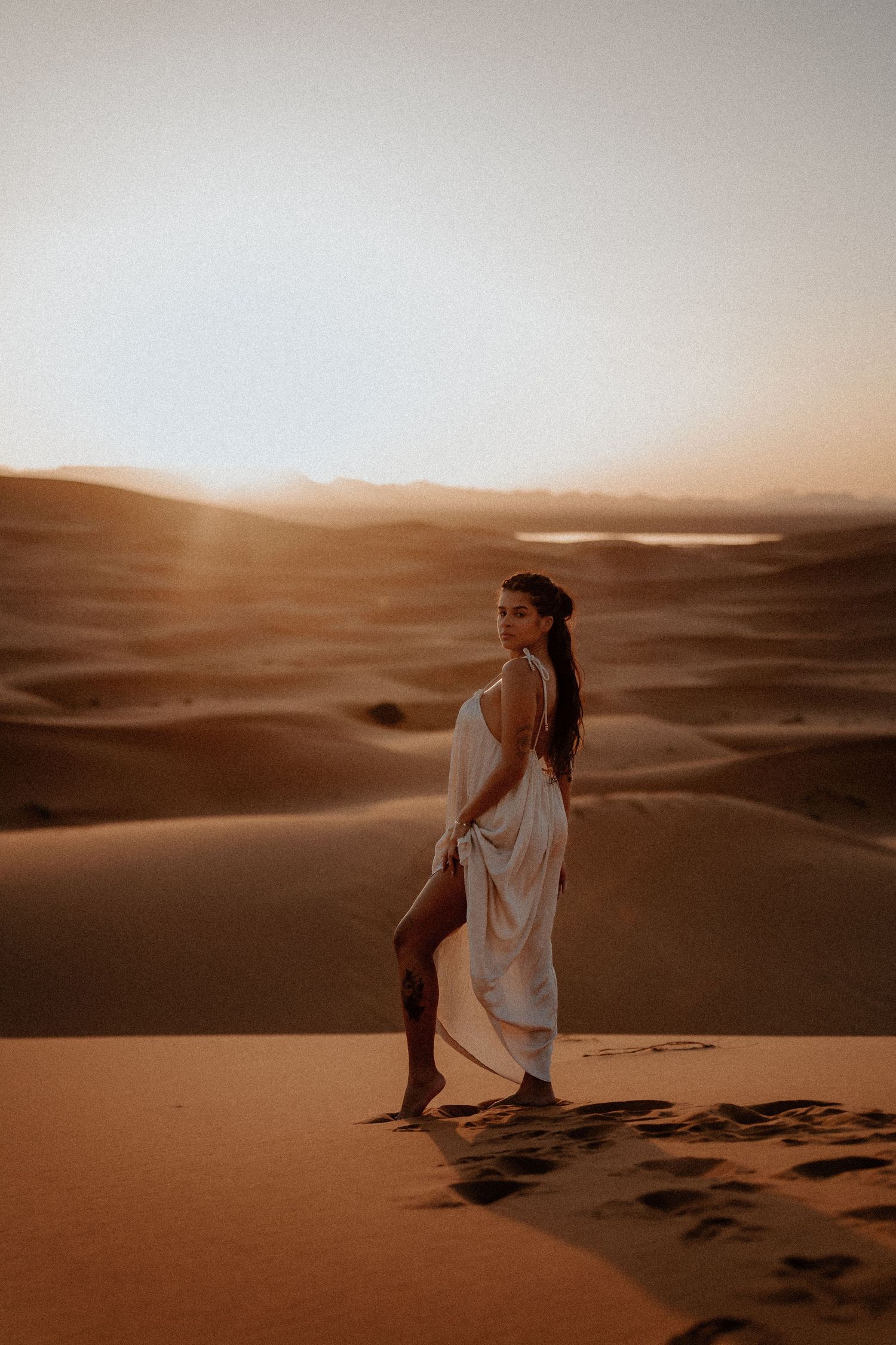 Person in white dress standing on desert dune at golden hour.