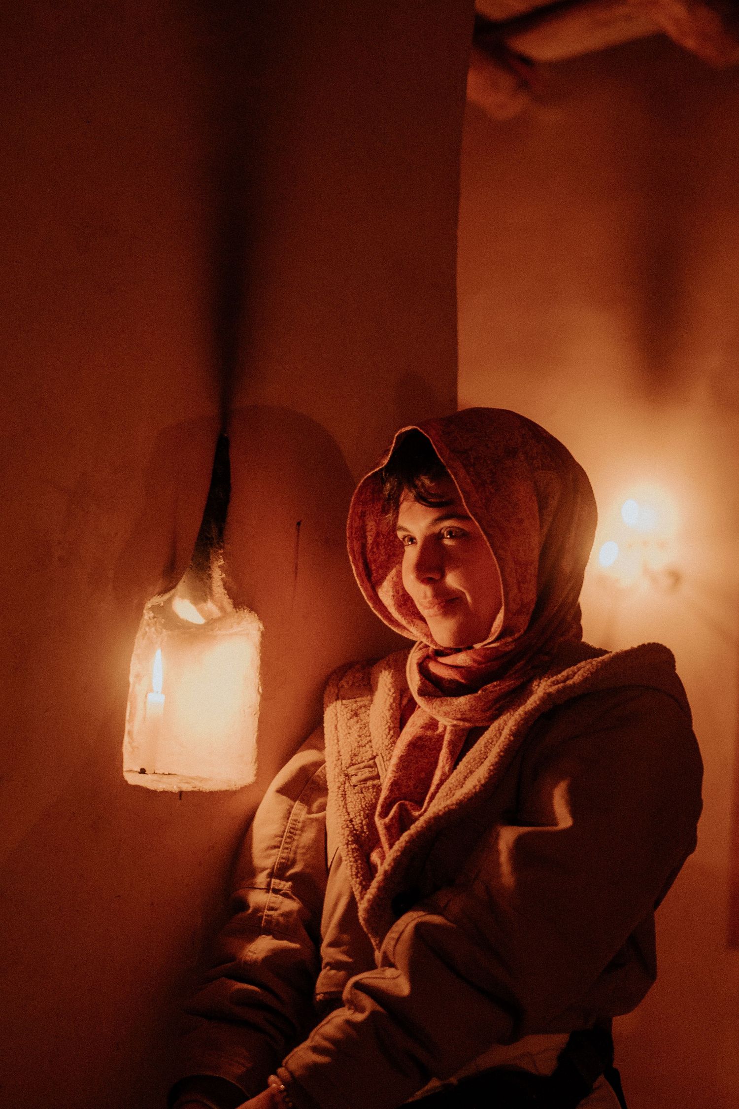 A person in traditional desert clothing sits by lantern light in a dimly lit room with warm orange tones.