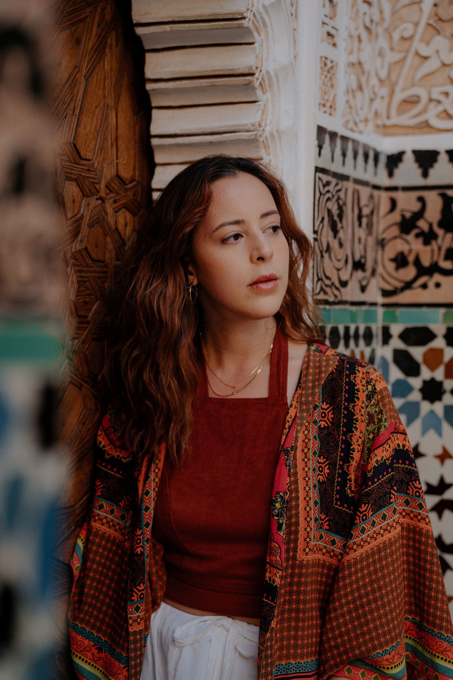 Bohemian style fashion with ethnic patterned cardigan and red top against decorative moroccan tiles.