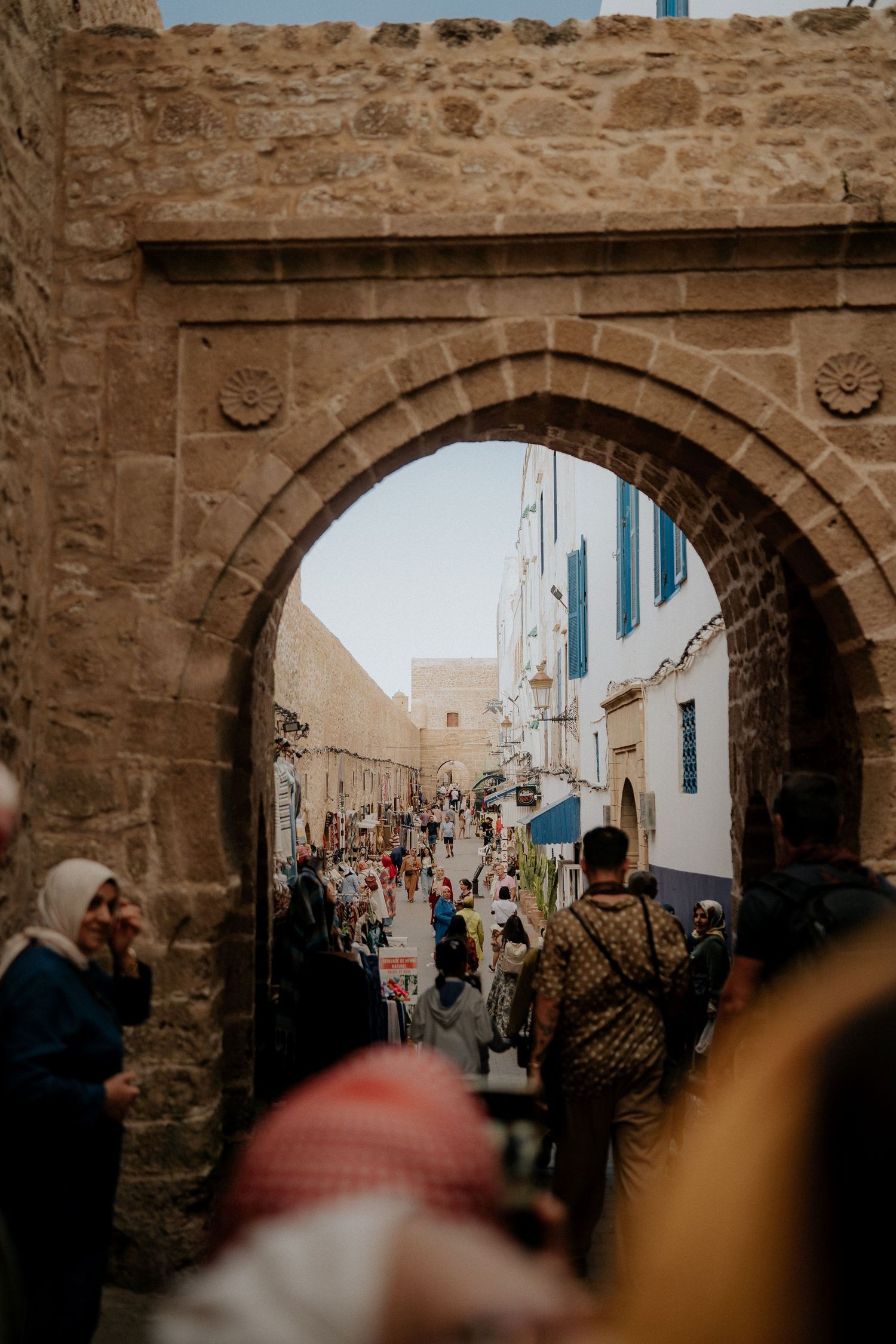 Bustling market street through stone archway in Moroccan medina.
