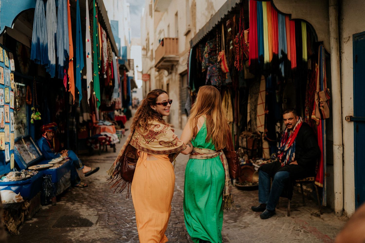 Narrow winding alleyways of a traditional Moroccan medina with colorful textiles and goods displayed in market stalls.