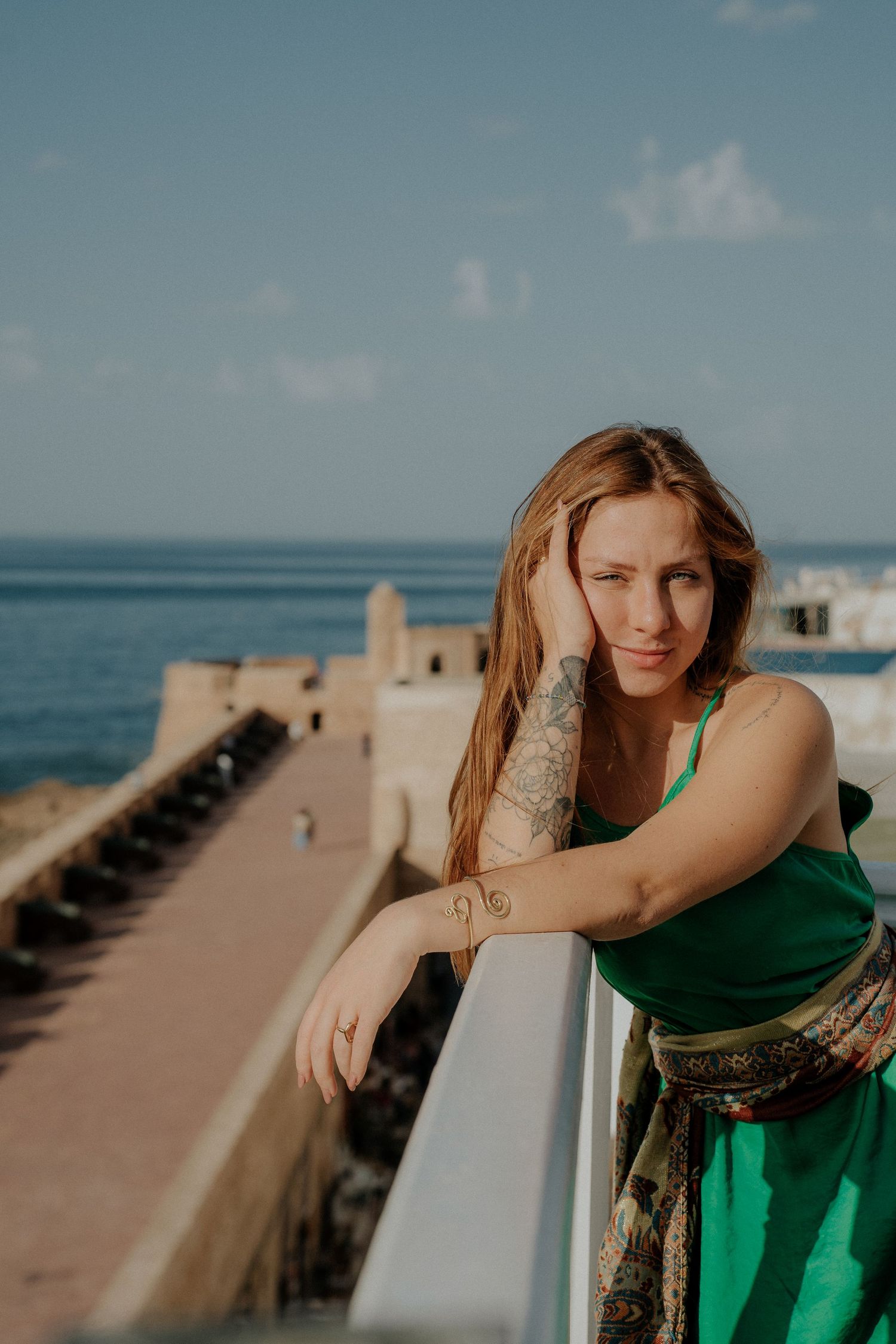 Ocean view along a concrete pier with green dress against bright blue sky and water.