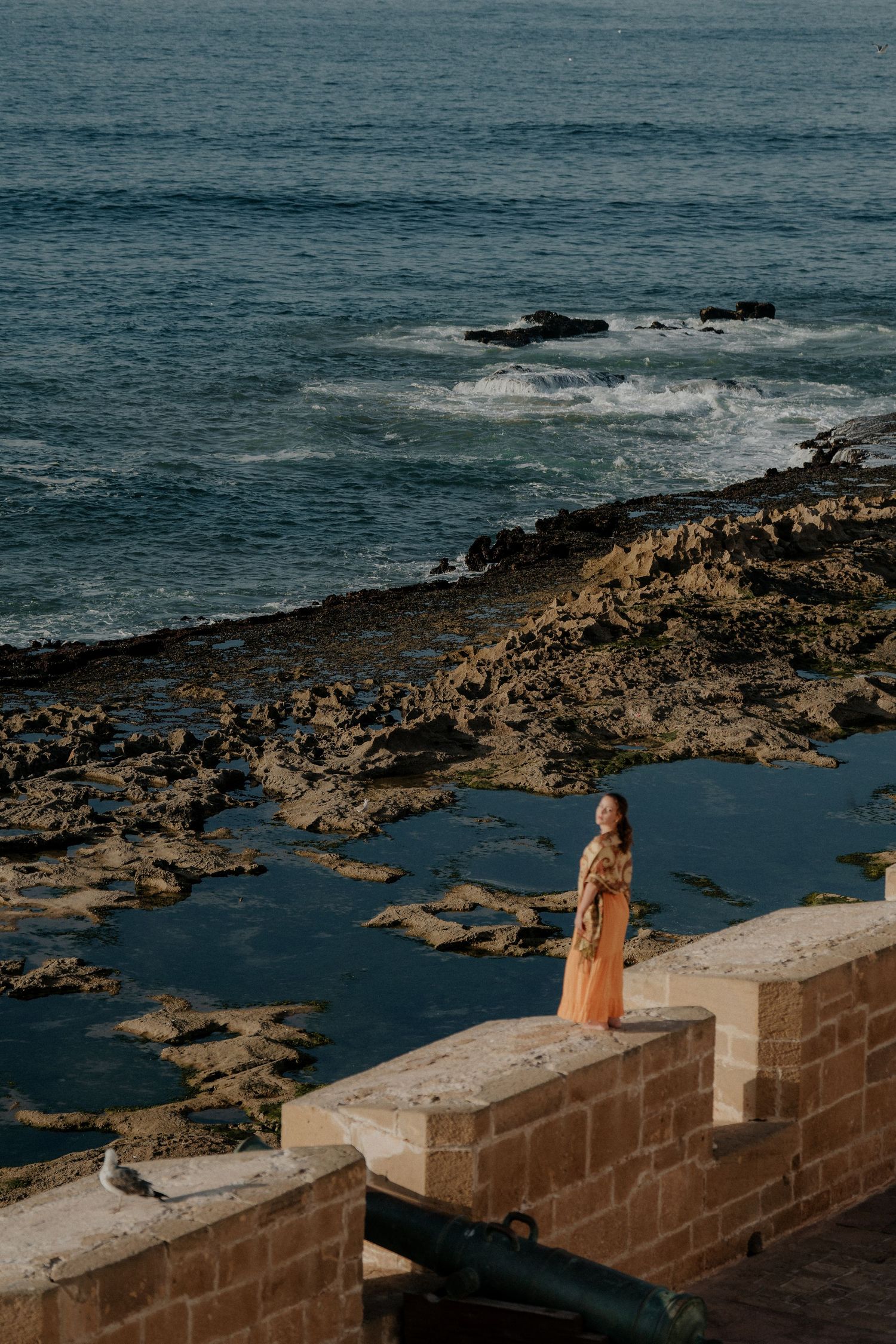 Rocky coastline with stone walls overlooking deep blue ocean waters.