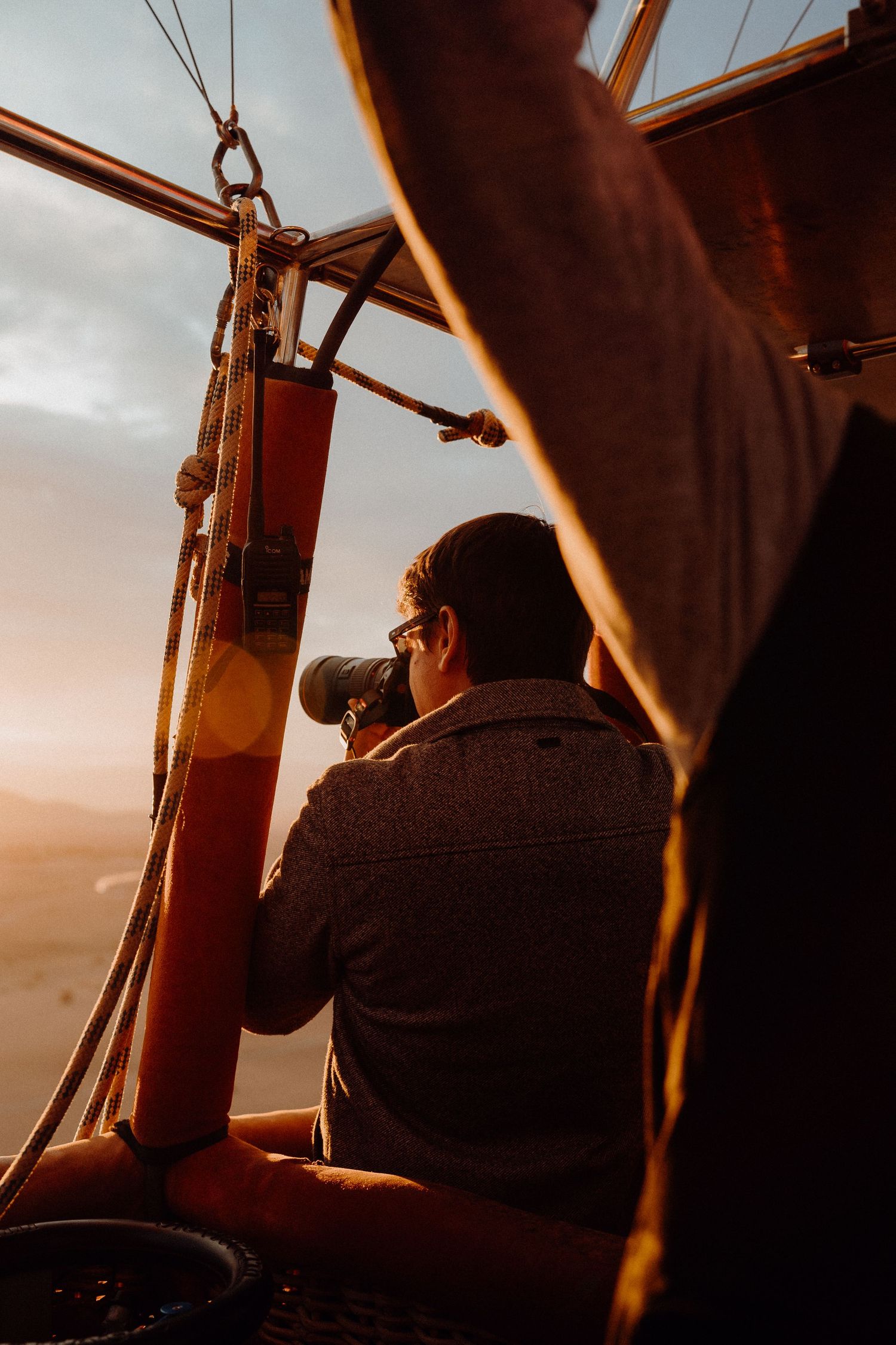 Photographer taking pictures from hot air balloon basket during sunset.