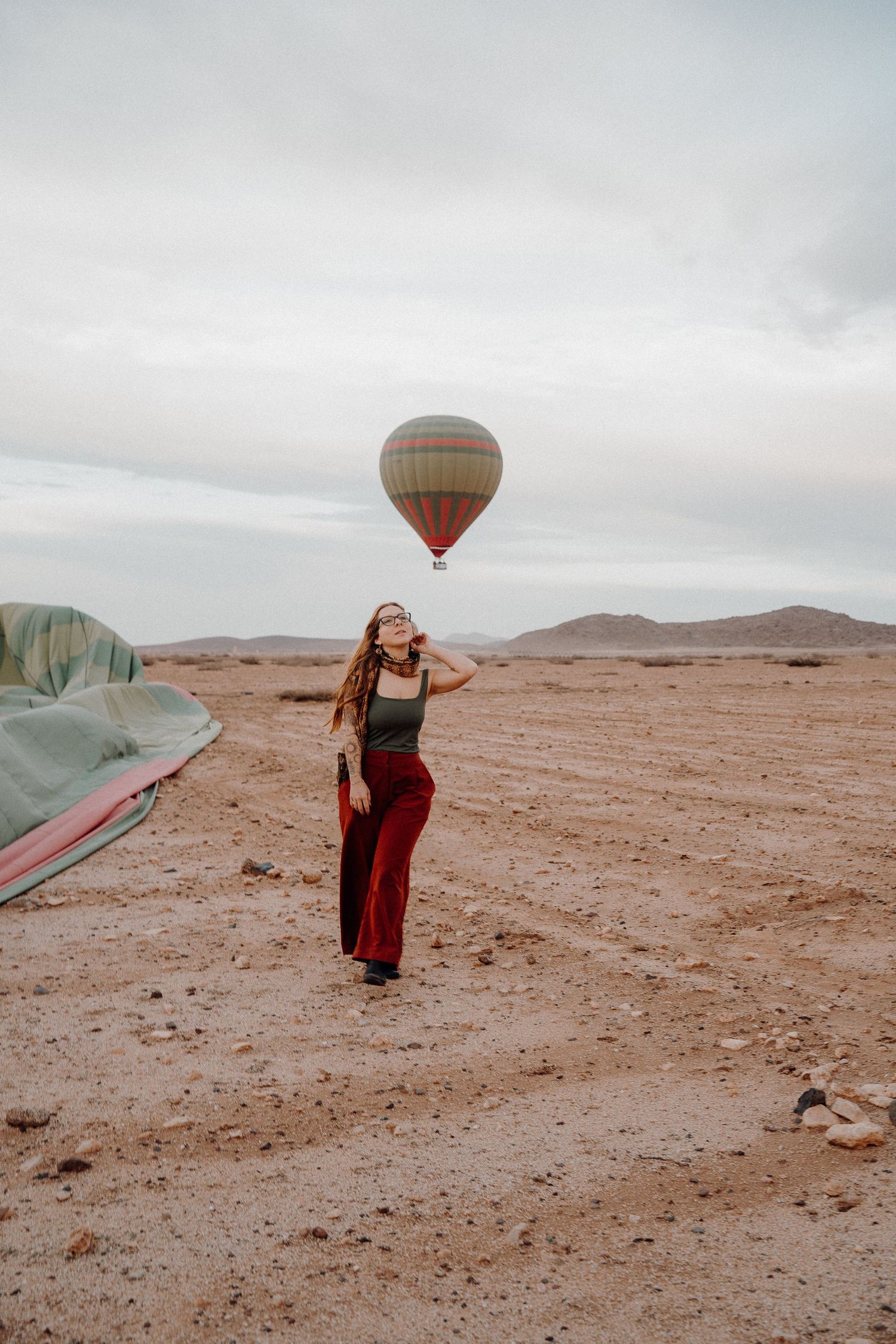 Desert traveler poses with hot air balloon floating in background.