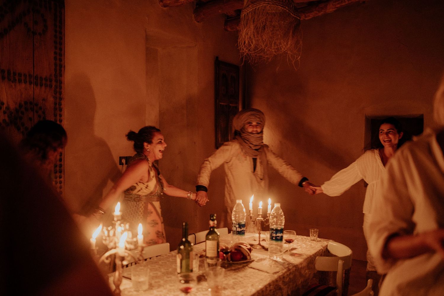 Group celebrating around candlelit table in rustic indoor setting with warm ambient lighting.