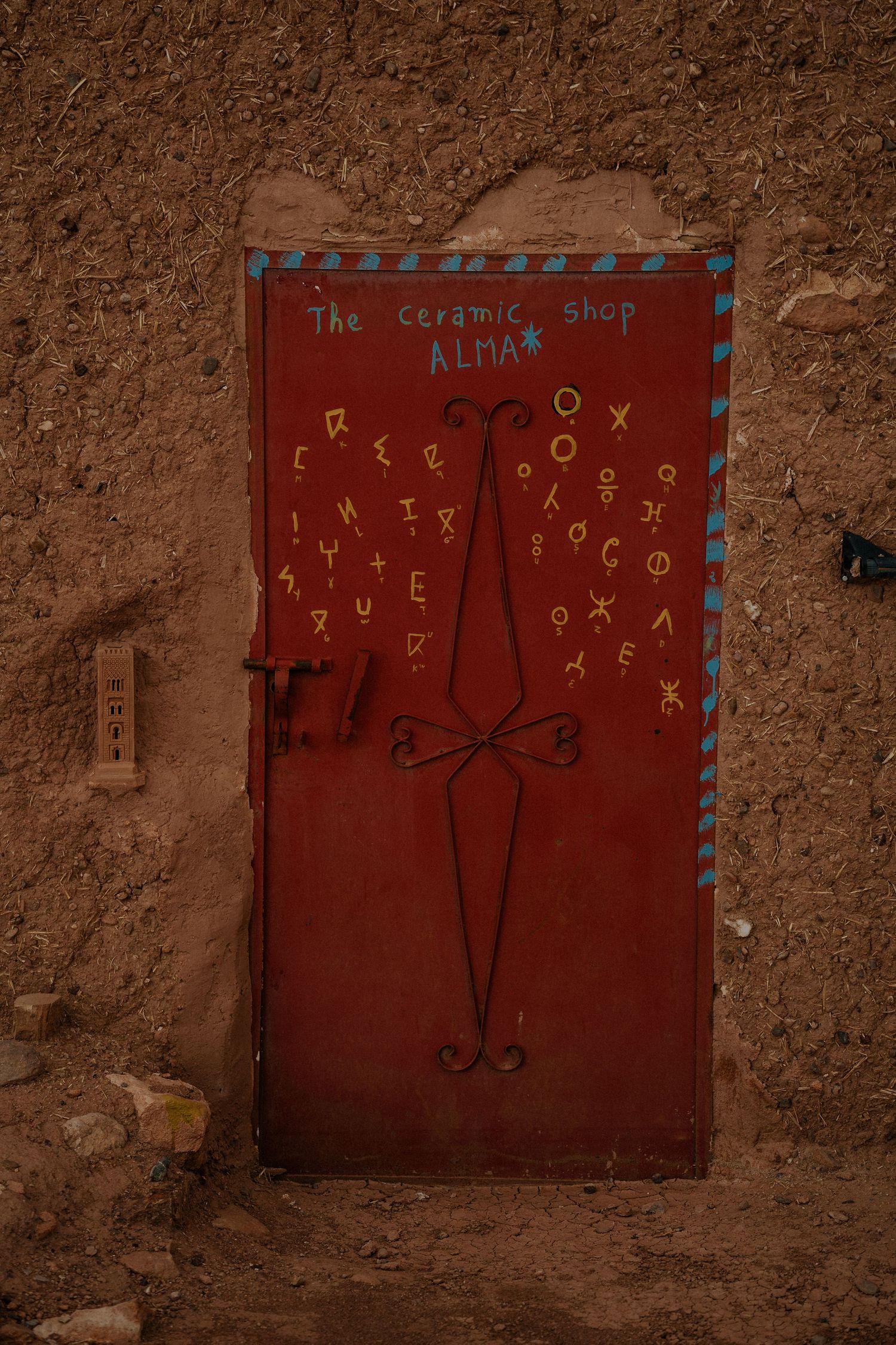 Red painted door with decorative symbols and text on weathered clay wall.