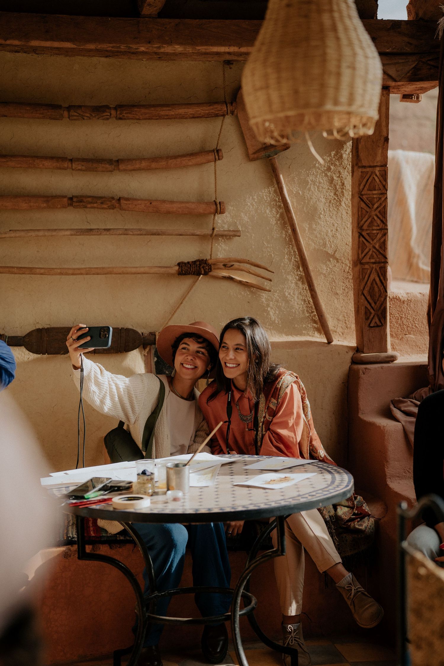 Friends taking selfie at cafe table in traditional Moroccan setting with natural light.