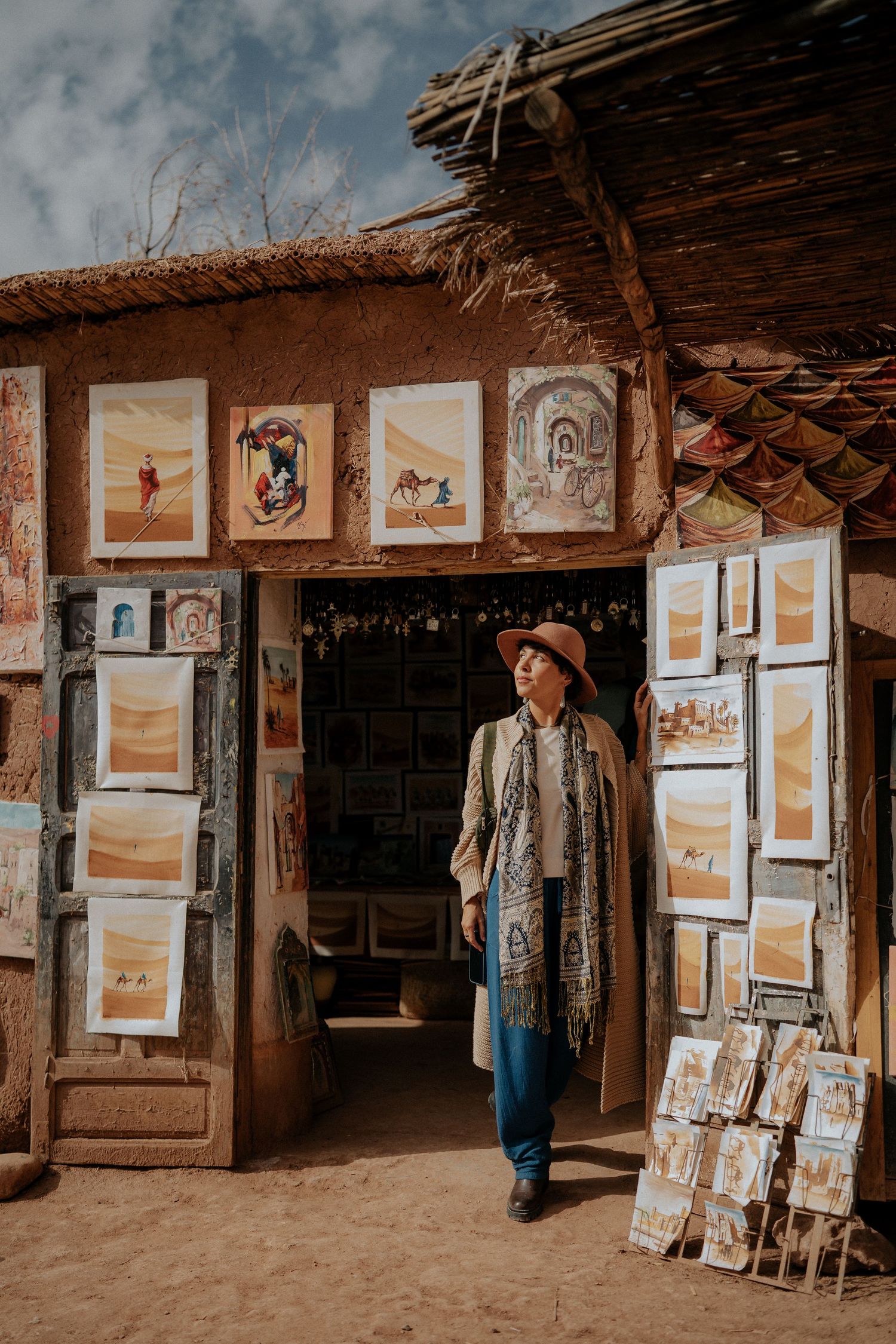 Art gallery entrance with framed paintings displayed outside adobe building in desert setting.