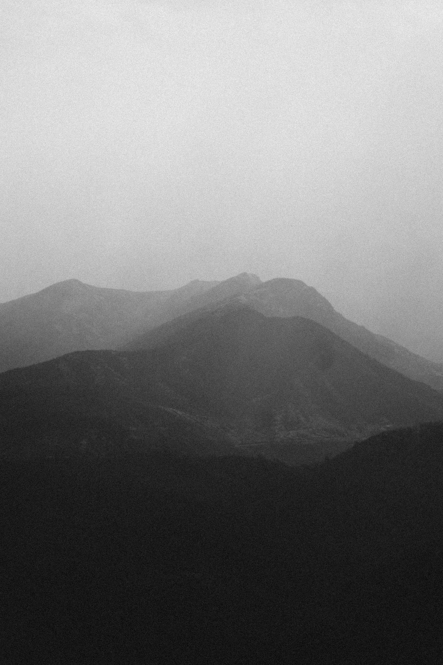 Black and white mountain landscape with misty peaks fading into foggy horizon.