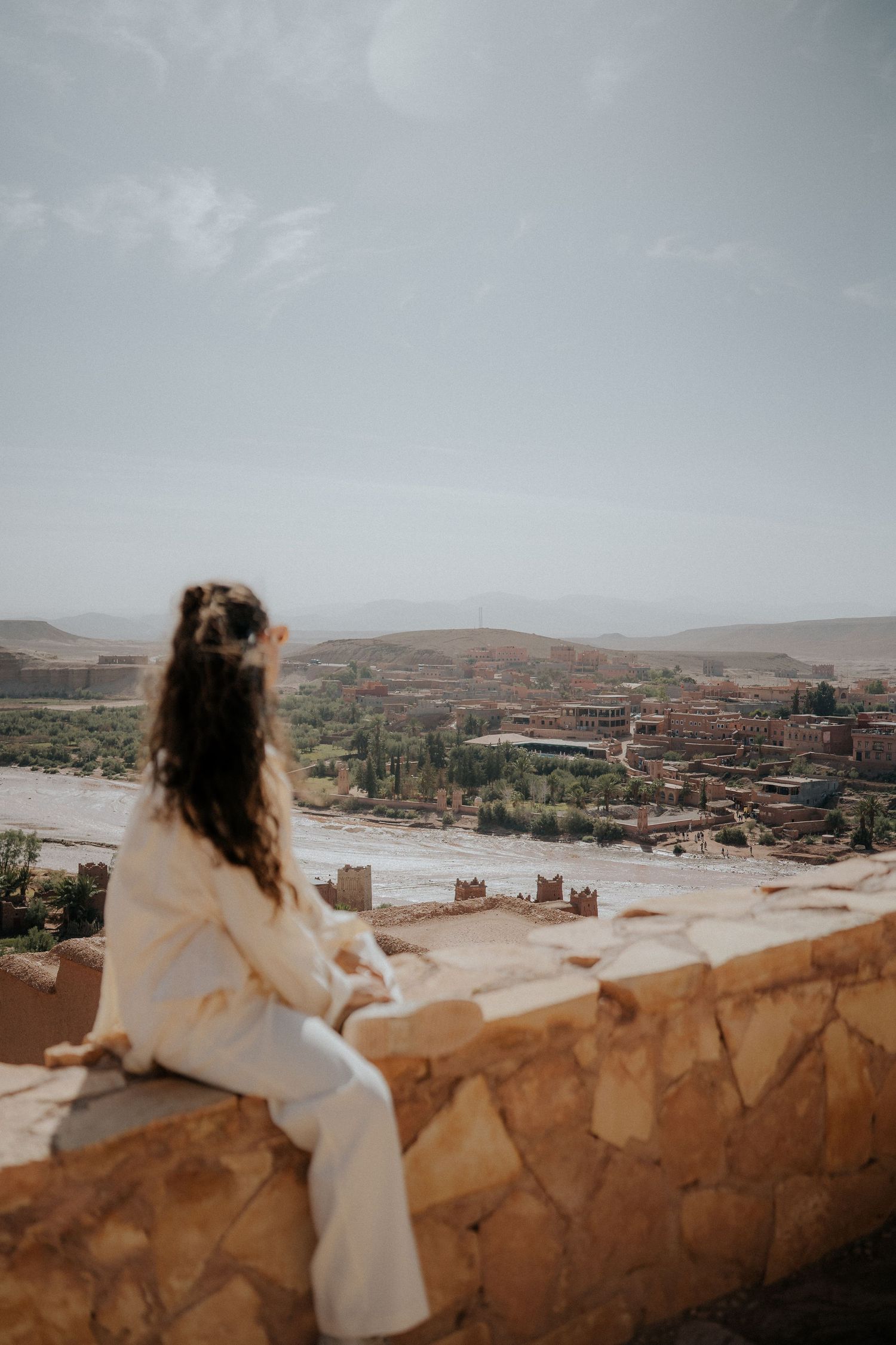 Panoramic view of historic kasbah overlooking river valley in Morocco's desert landscape.