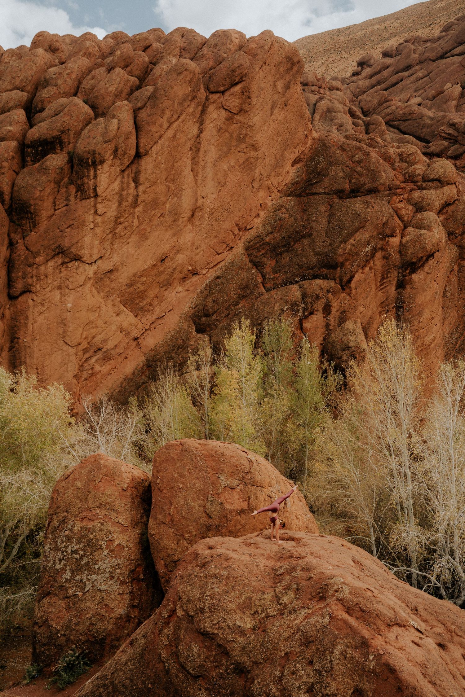Dramatic red rock formation in Moroccan desert with green vegetation at its base.