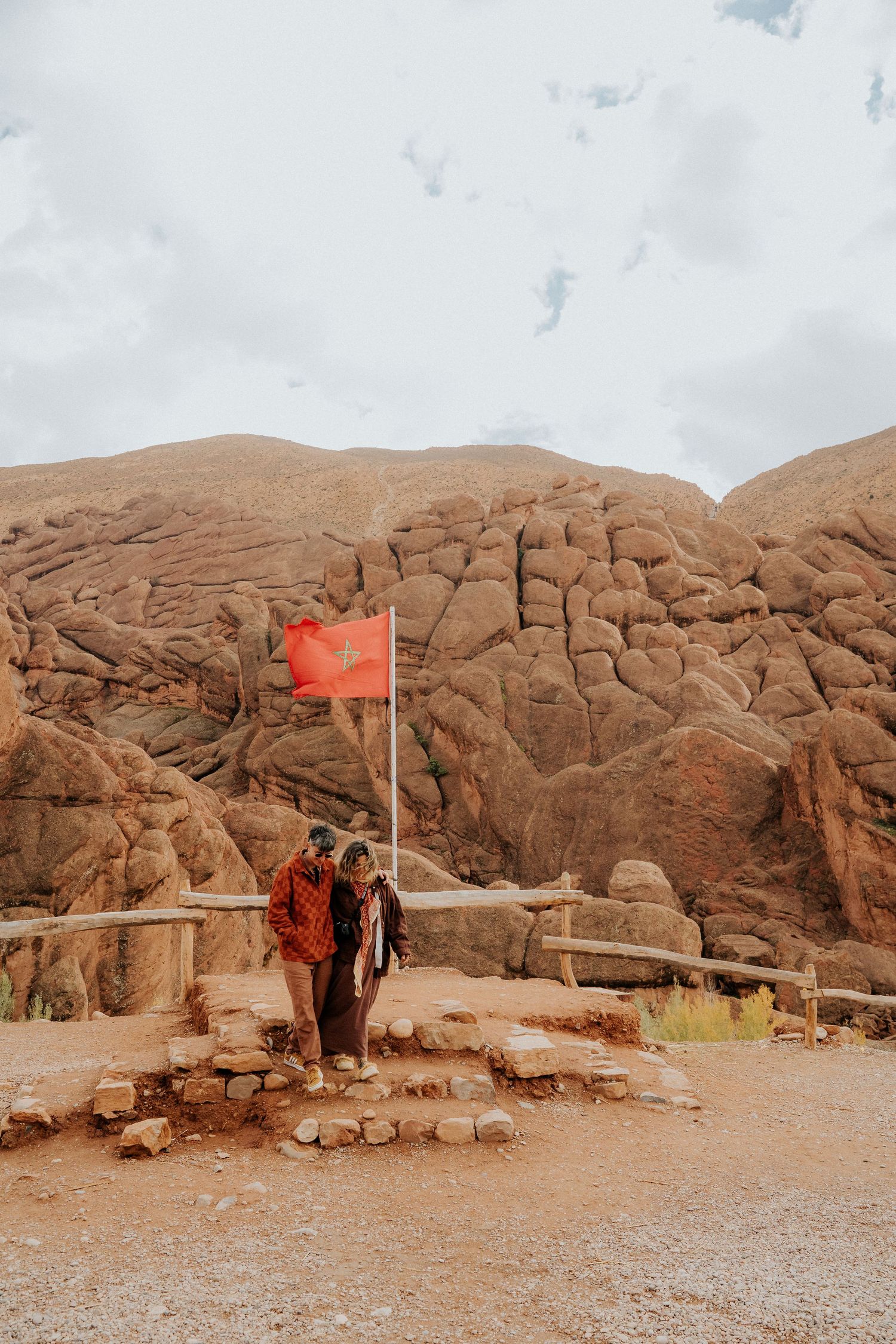 Red rock desert landscape with Moroccan flag and stone pathway.