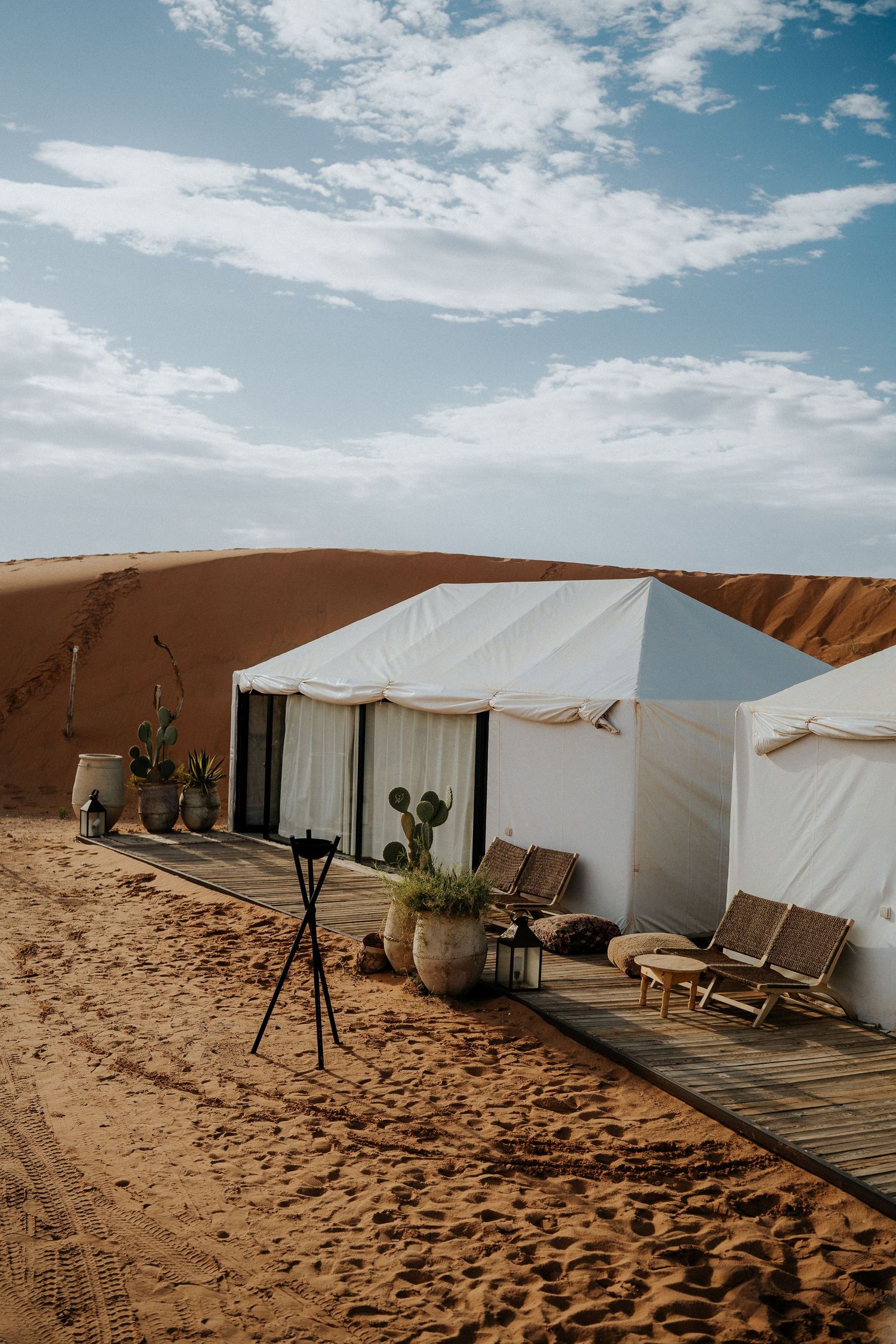 White canvas tents set up against sand dunes create a luxury desert camp experience under blue skies.