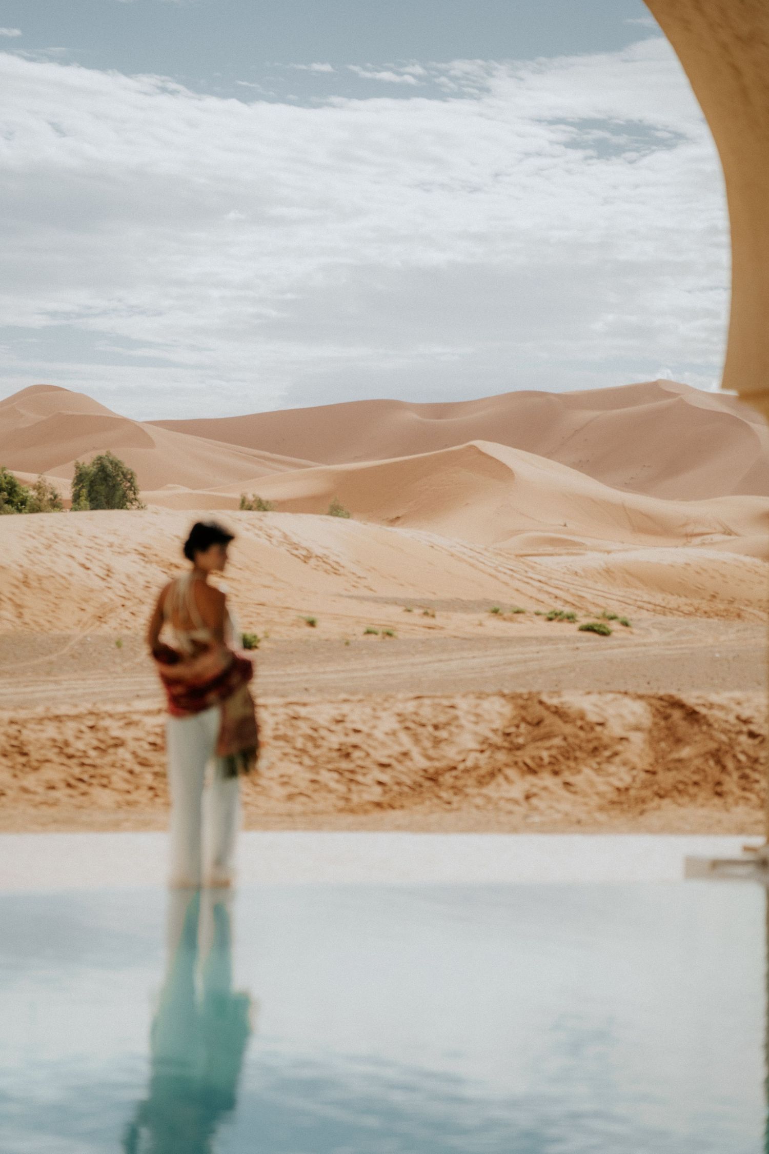 Desert landscape with rolling golden sand dunes stretches to the horizon under a bright blue sky.