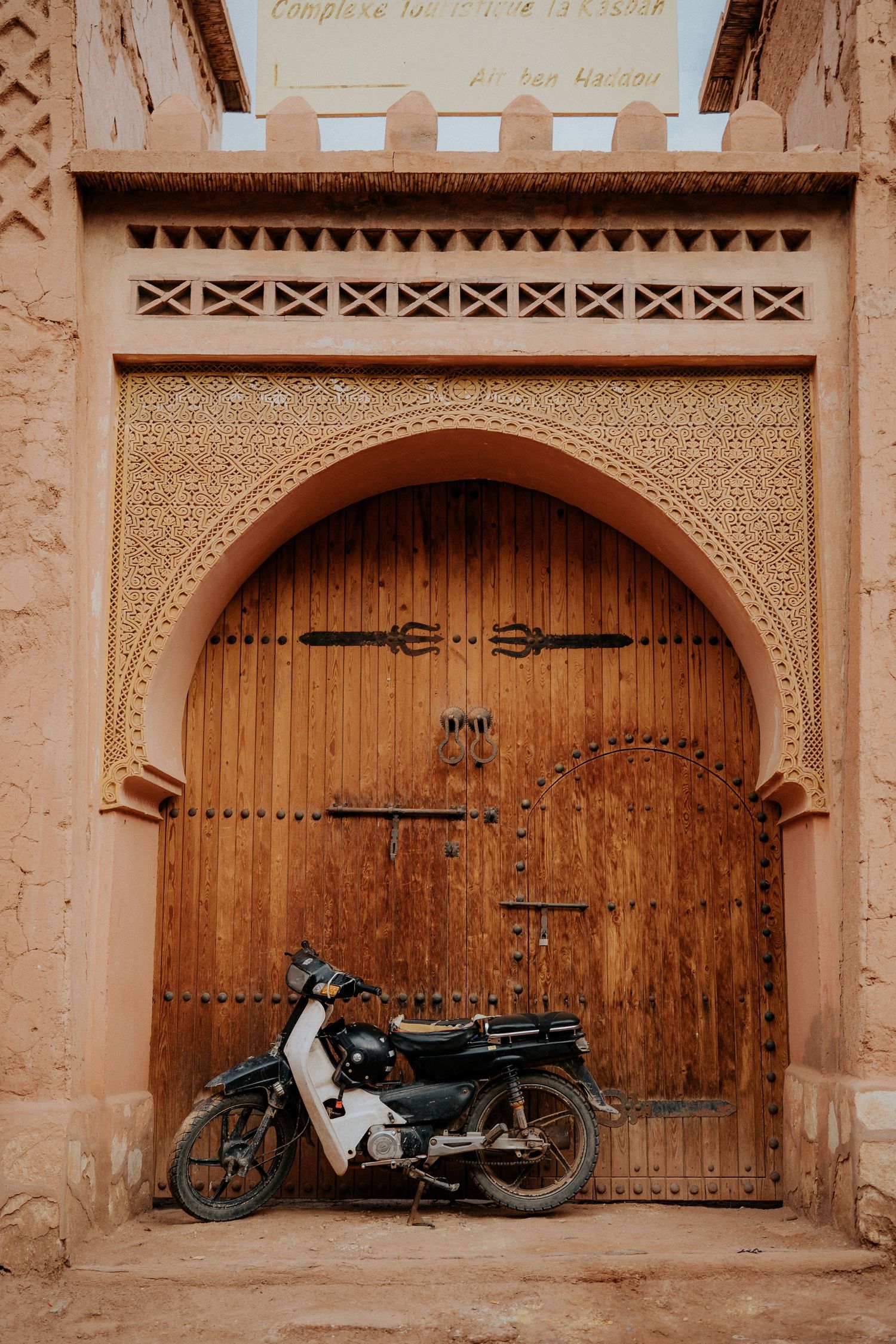 Vintage motorcycles parked in front of ornate wooden doors with traditional Moroccan archways.