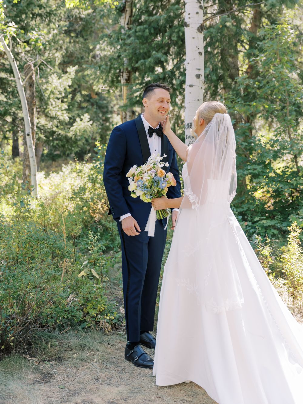 A couple shares a tender moment amongst trees during their outdoor wedding photography session.