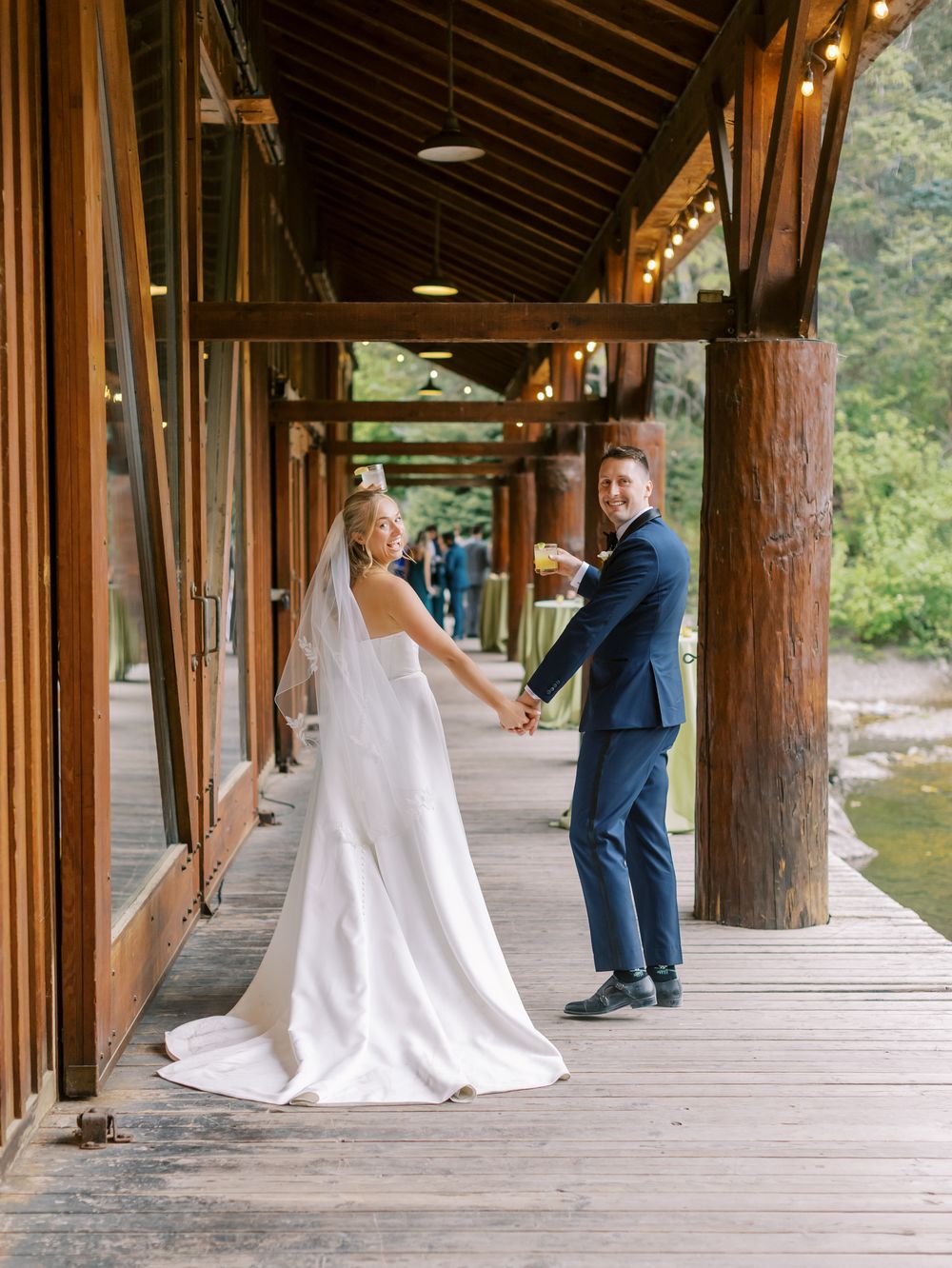 A couple in wedding attire share a moment on a rustic wooden porch with log columns.