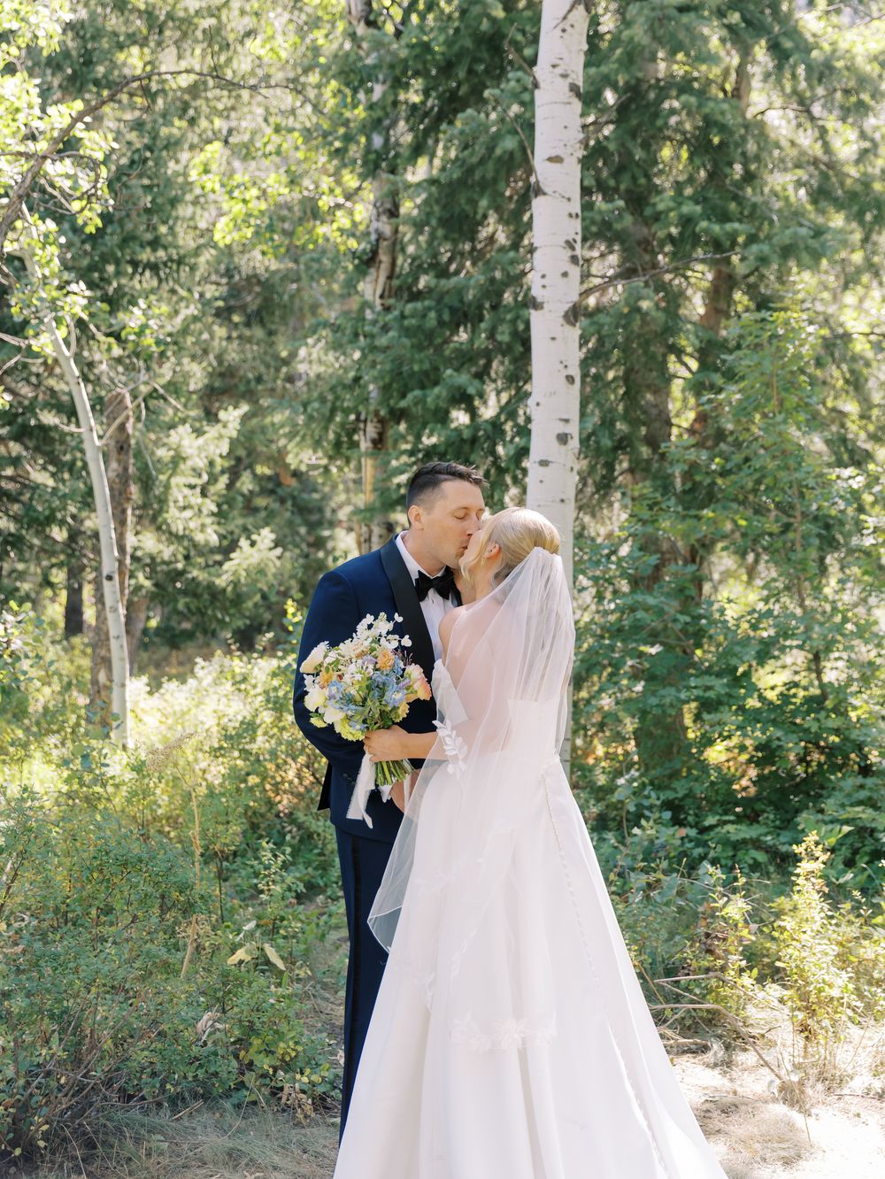 Newlyweds share an intimate moment among white birch trees in a dreamy forest setting.