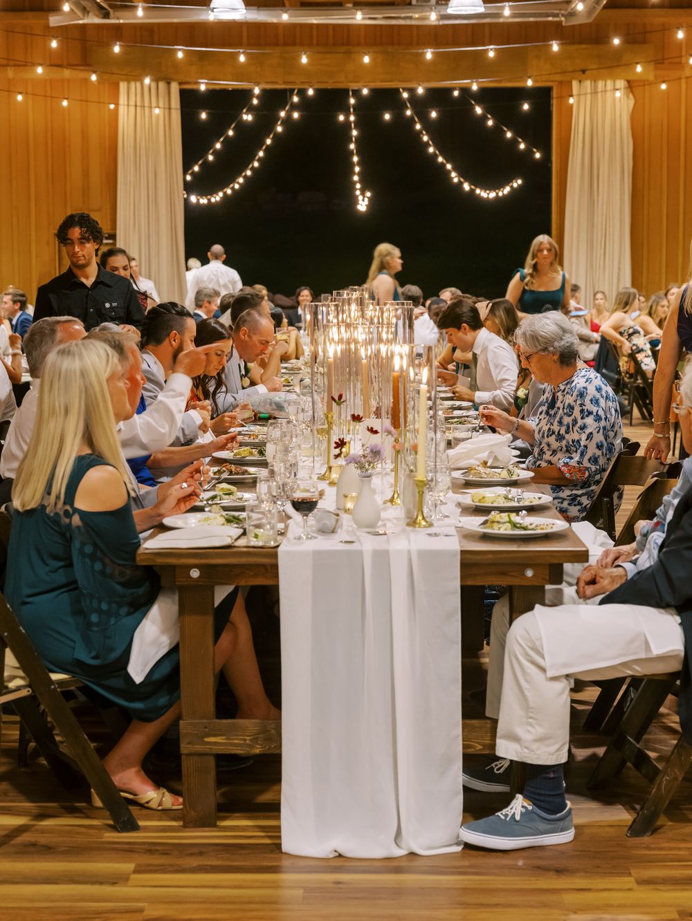 Wedding reception dinner setup with elegant white tablecloths and string lights creating a warm ambiance.