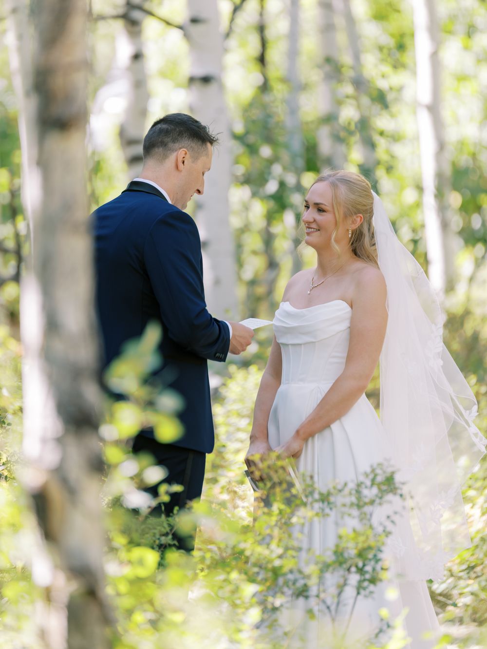 Bride and groom share tender moments in a serene birch forest on their wedding day.