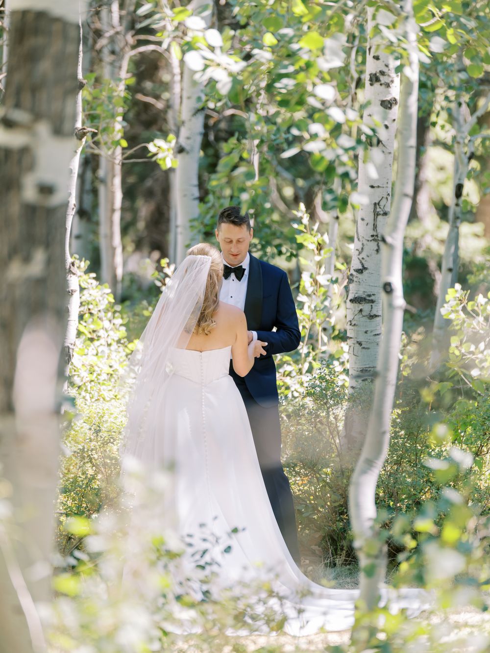 Wedding couple enjoying a romantic moment surrounded by sunlit aspen trees during their first look.