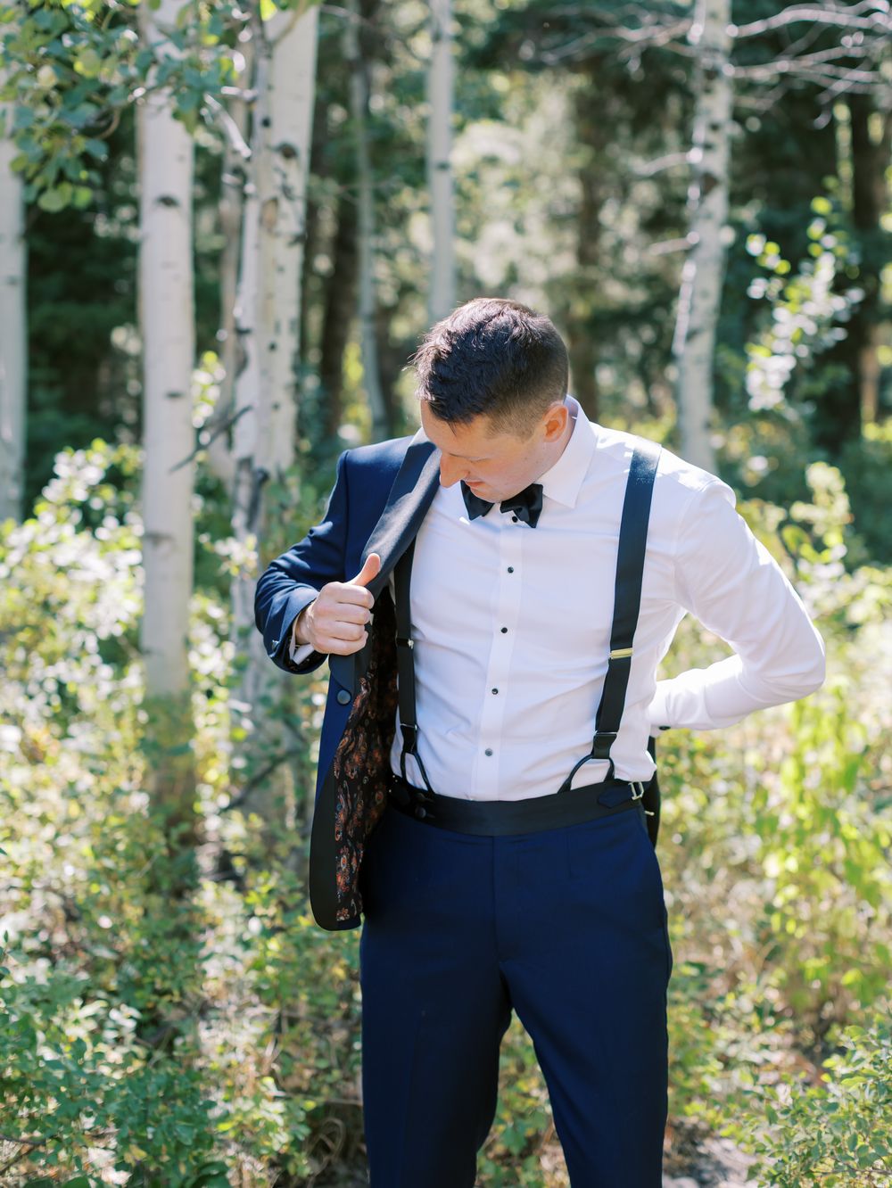 Formal attire details showing navy suspenders and bow tie against white shirt in aspen forest.