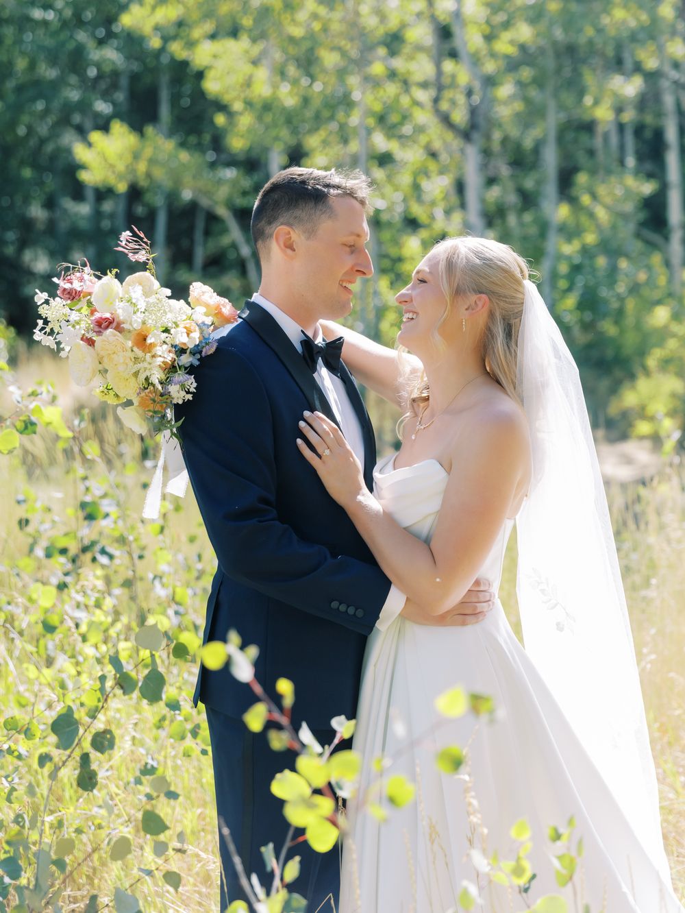 A romantic wedding couple shares tender moments in a sunlit aspen grove during their outdoor photo session.