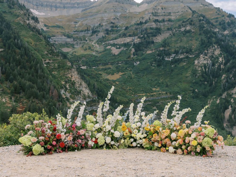 A stunning floral arrangement with delphinium spikes sits against a dramatic mountain backdrop.
