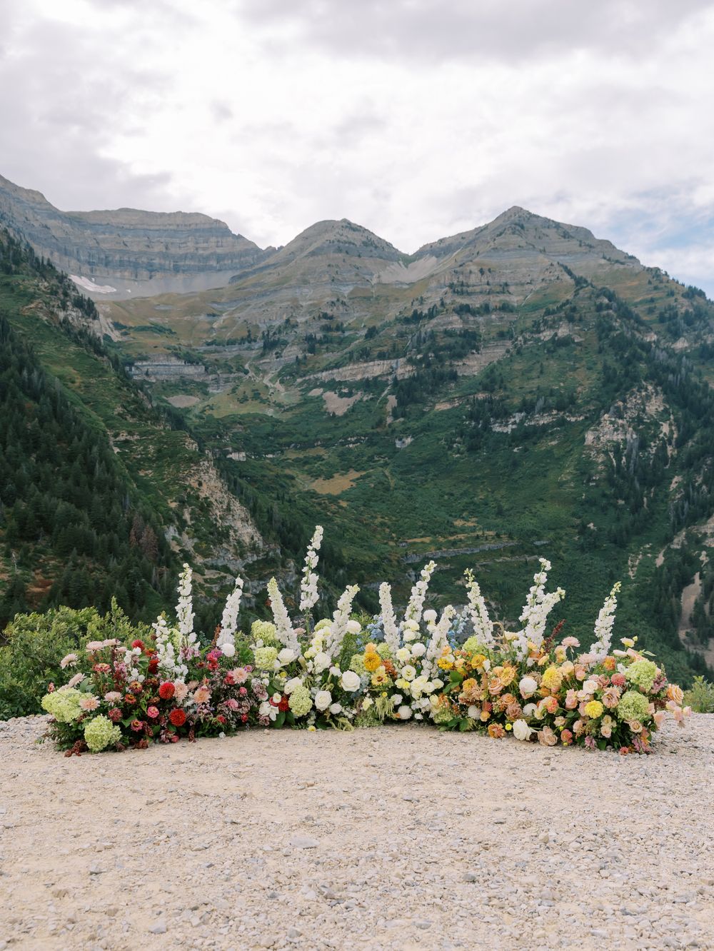 Elegant wedding altar flowers featuring tall white delphiniums and mixed blooms in front of mountain scenery.