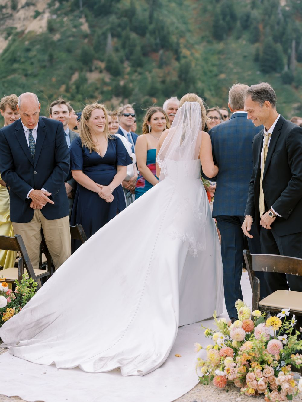 An outdoor wedding ceremony set against a mountainous backdrop with elegant white decor.
