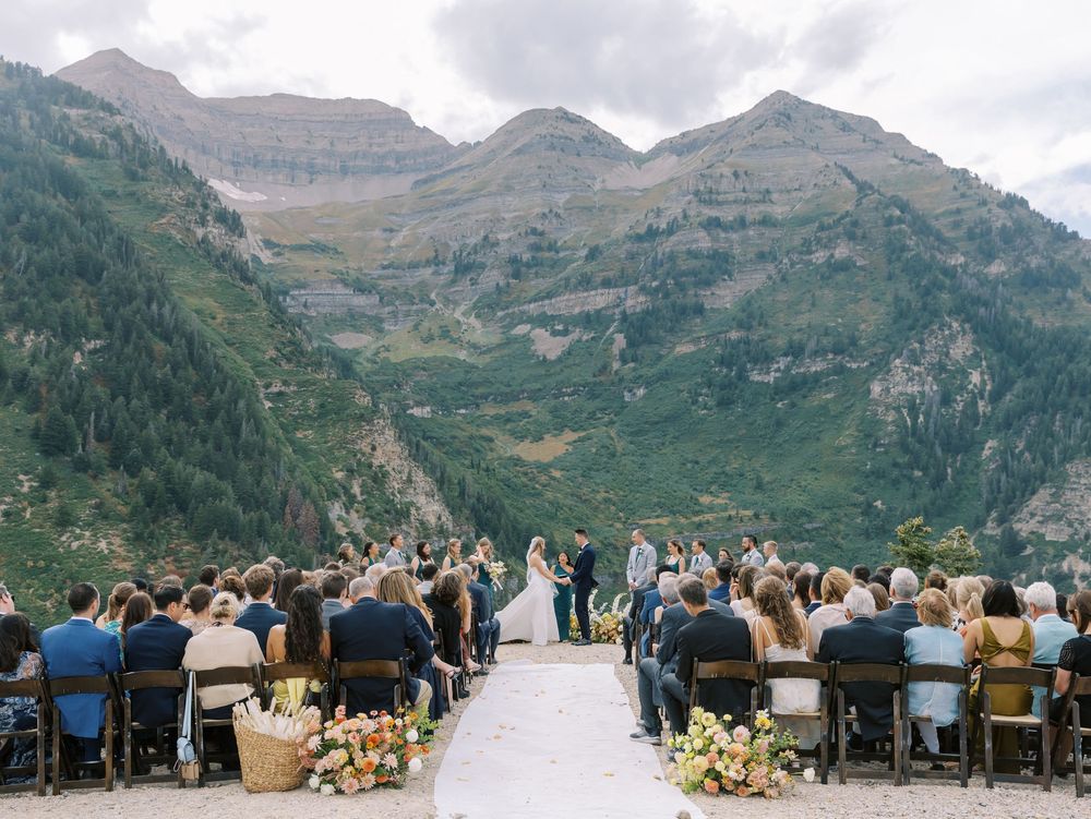 A mountain wedding ceremony with guests seated in rows facing majestic peaks in the background.