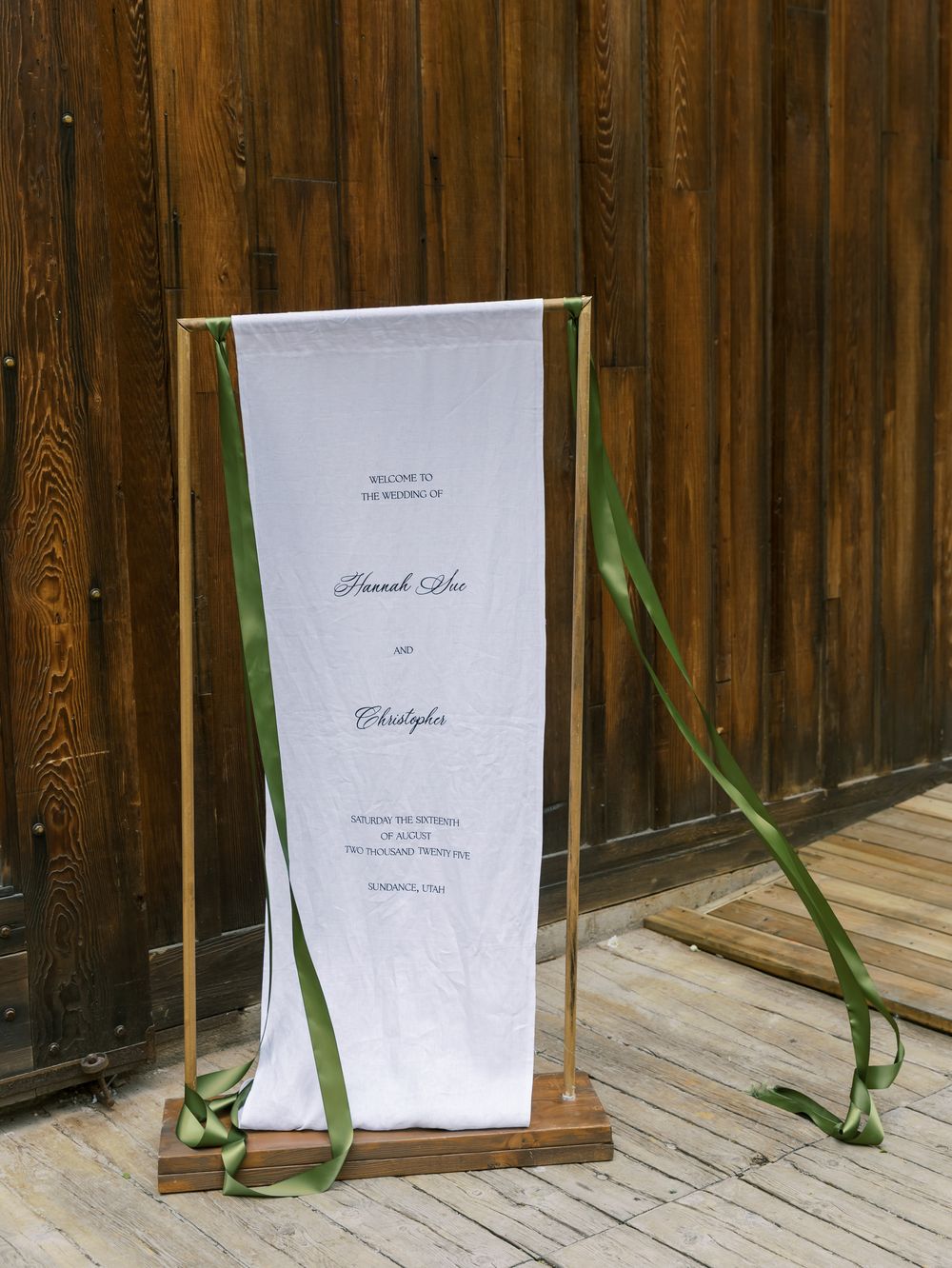 White wedding ceremony programs displayed on wooden stands against a rustic wood panel wall.